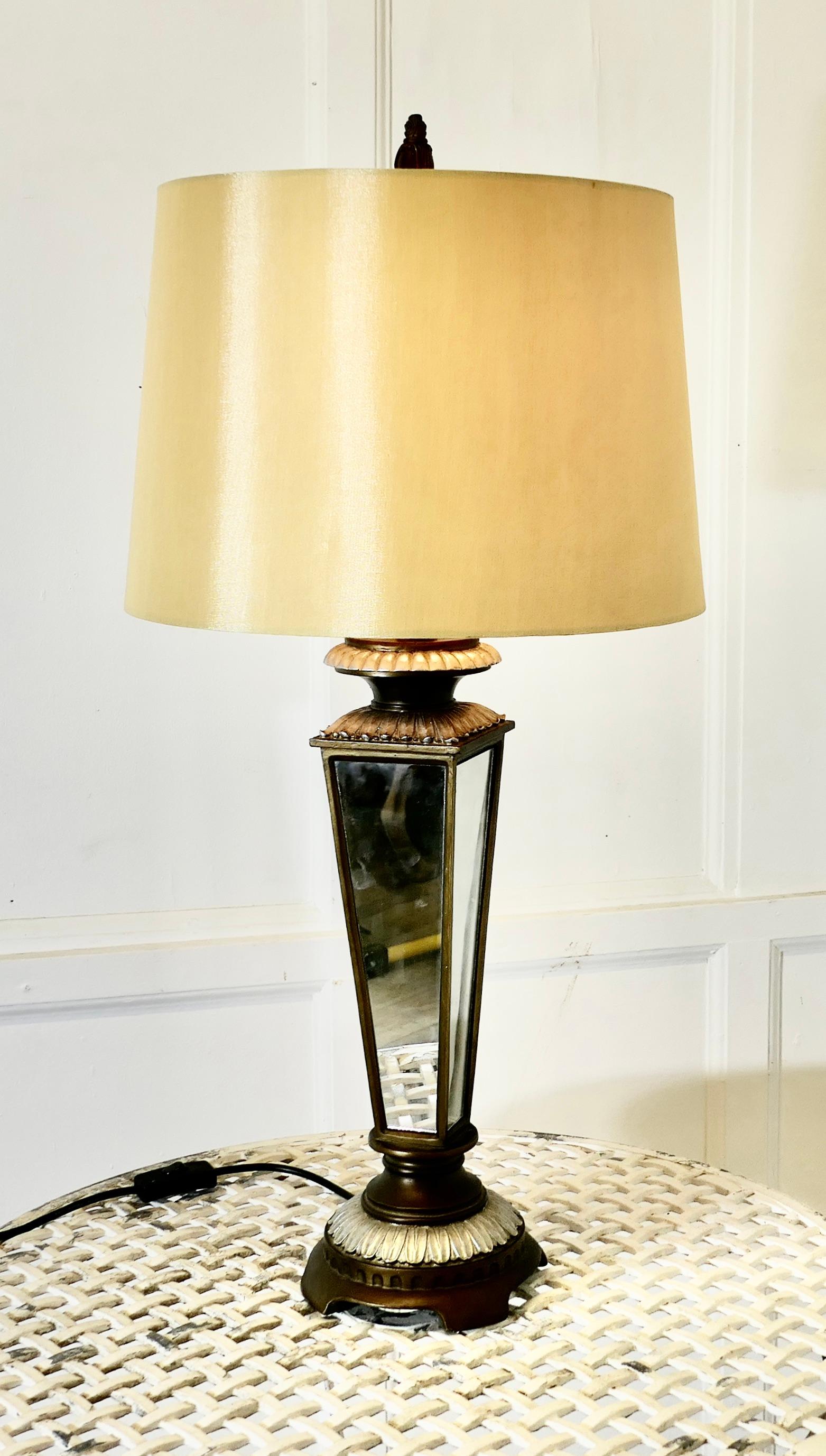 An Art Deco Style Mirror Table Lamp 

The lamp stands on a circular bronzed and silvered foot, it has a 4 sided mirrored central column set in brass with further decoration matching the base  

This is a stunning lamp and it has a gold linen shade