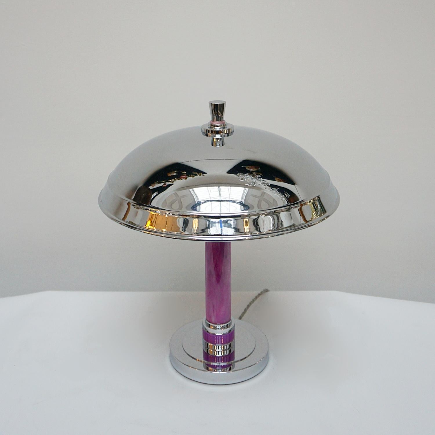 A tall Art Deco table lamp with a domed shade. Tubular, purple coloured bakelite stem with bands of chromed metal and alternating discs of bakelite. Set over a flat base. Metal finial to top.

Dimensions: height 41cm, diameter of shade: 35cm,