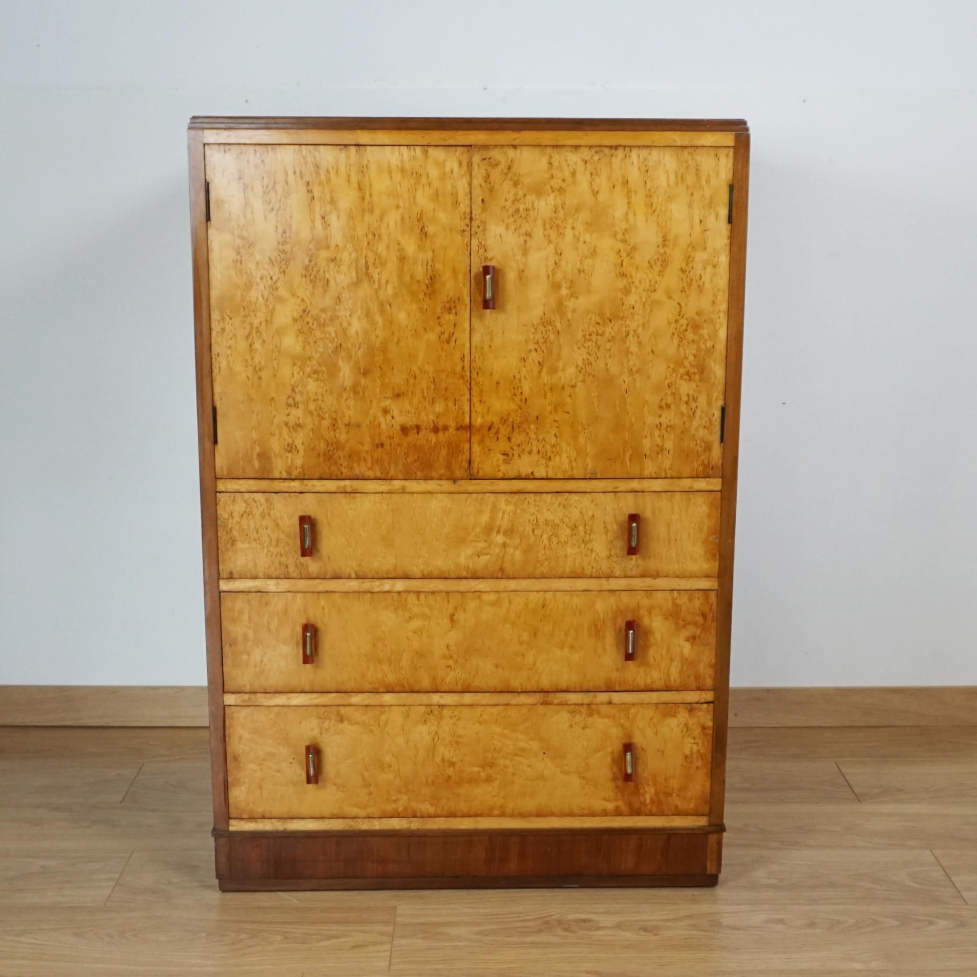 An Art Deco Tall Boy / Linen Cupboard. Karelian birch and figured walnut veneer. Upper section with two interior shelves and three lower drawers. Original bakelite and chromed metal handles. 

Dimensions: H 113cm W 75cm D 52cm
