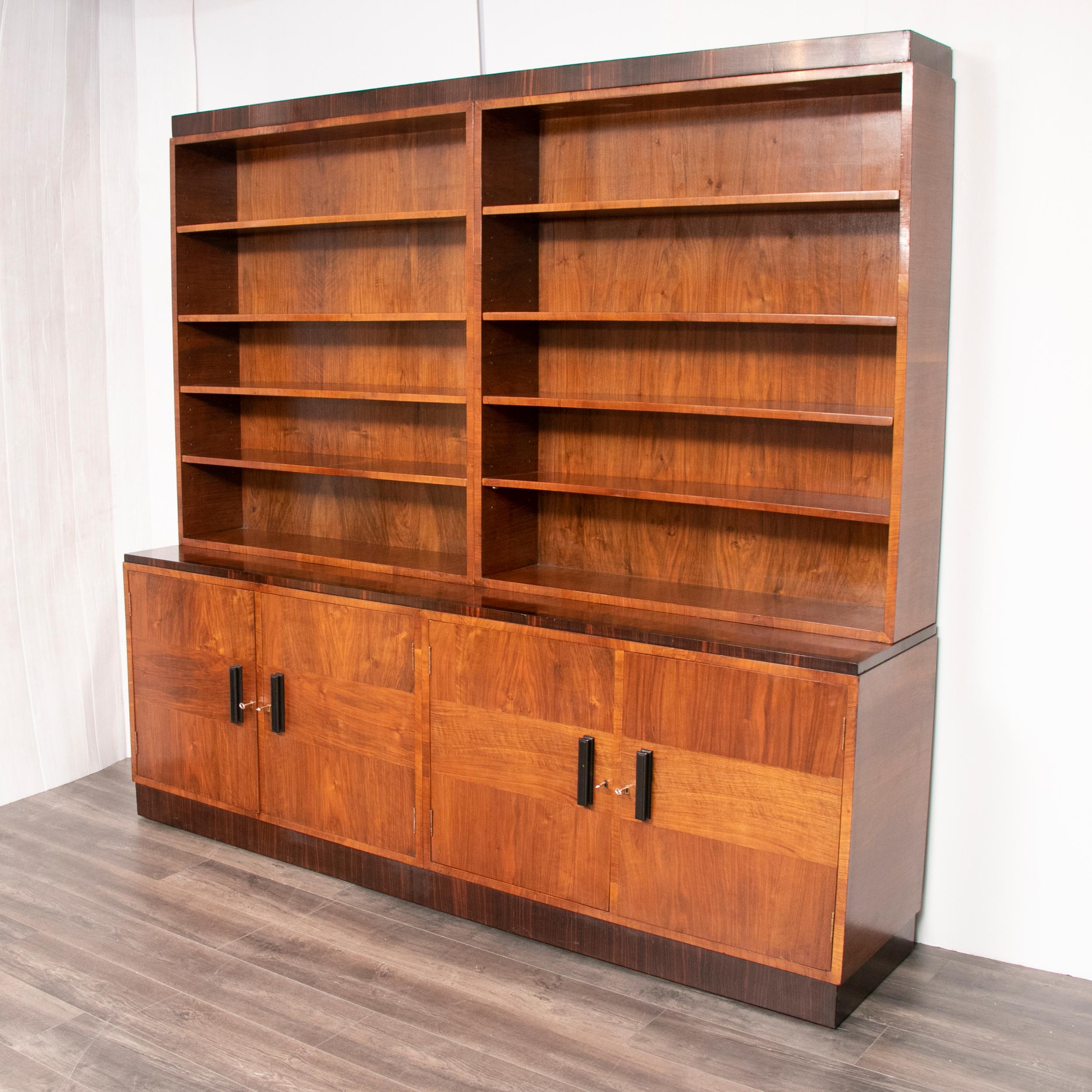 An Art Deco bookcase with open top and cupboard base enclosing shelves featuring crossbanding throughout and ebonized handles, circa 1930.