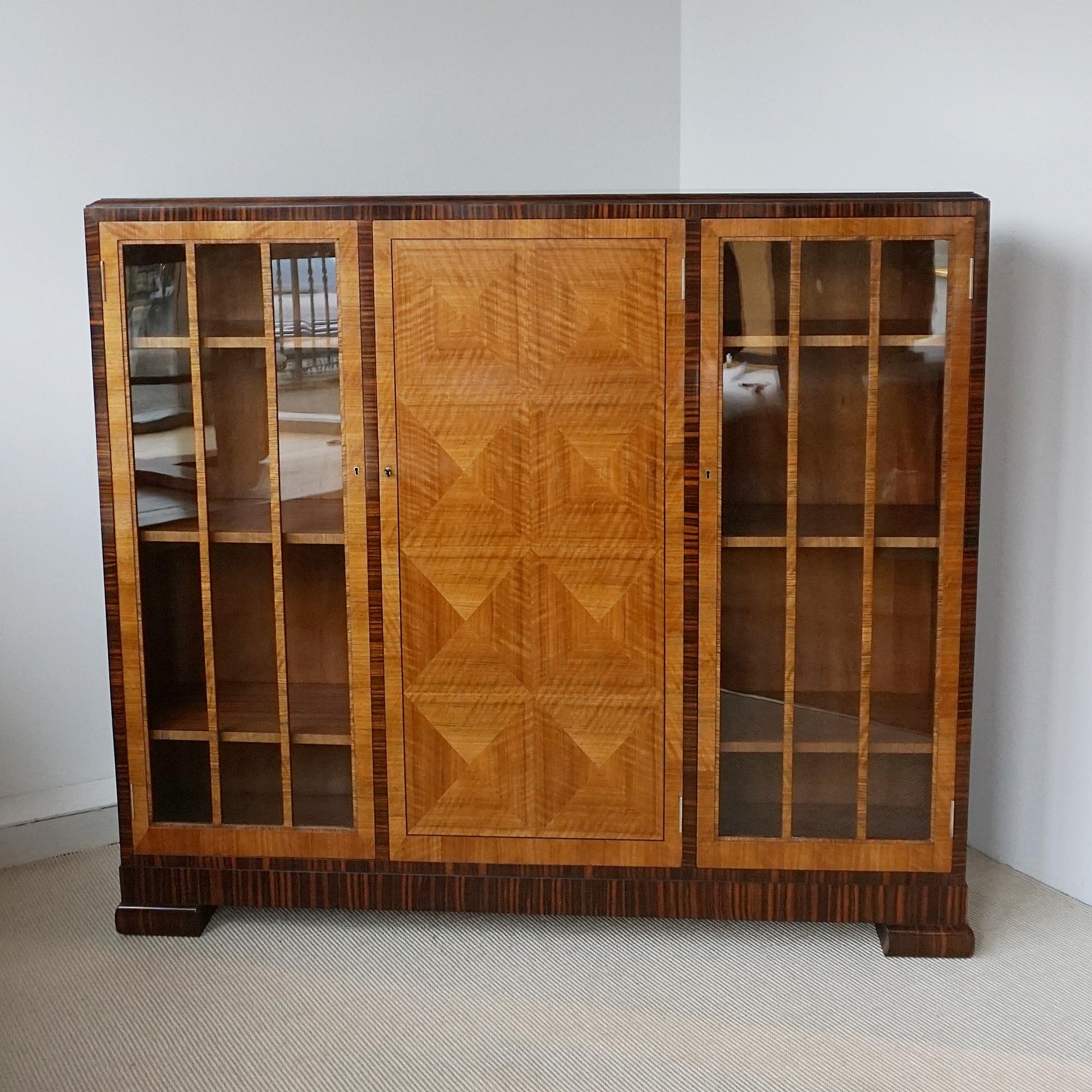 An Art Deco cabinet by Heal's of London. Central figured walnut veneered section with glass fronted doors to either side. Macassar ebony and figured walnut veneered throughout. 'Heals and Son' label to inside central cabinet door, with 'Richardson