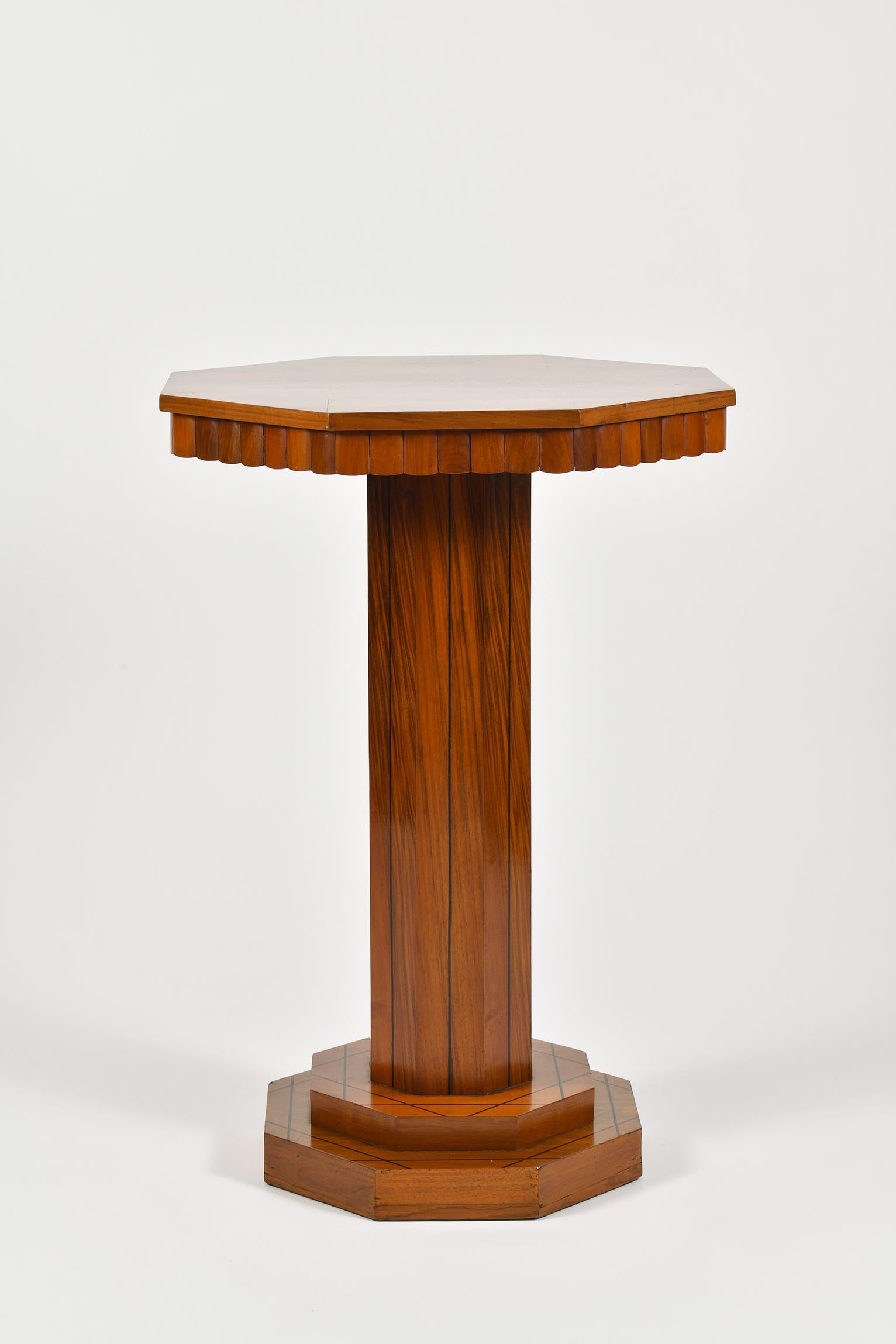 An Art Deco walnut and ebonised tall side table, the octagonal column stem resting on a double stepped plinth, supporting a star marquetry top with scalloped edges.
France, circa 1930.