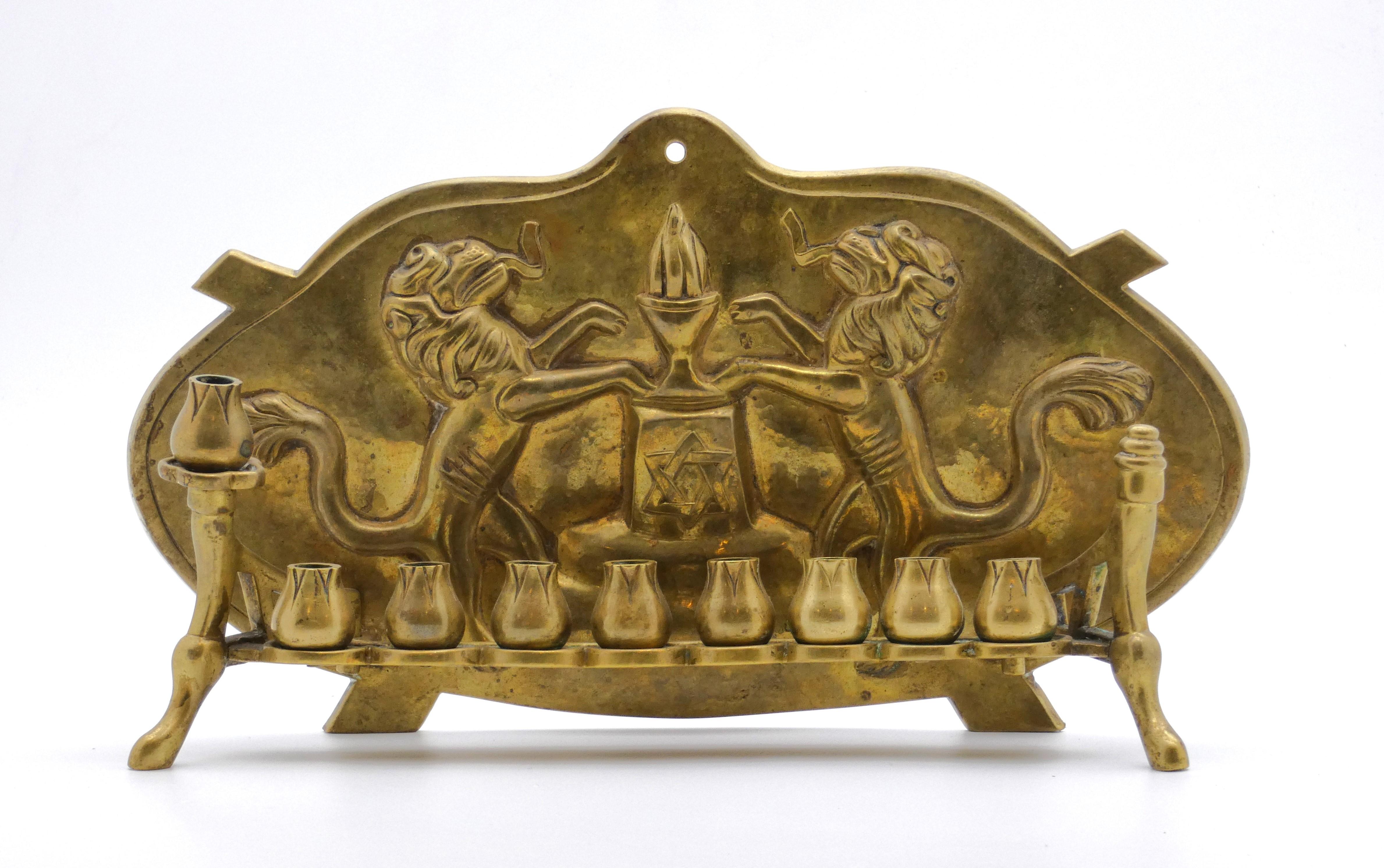 This splendid German Hanukkah Lamp suggests the Arts and Crafts style or even the unique Art Nouveau fashion. 

Backplate presents two rampant Lions of Judah with their tongues protruding, each with an extended front paw resting on a burning incense