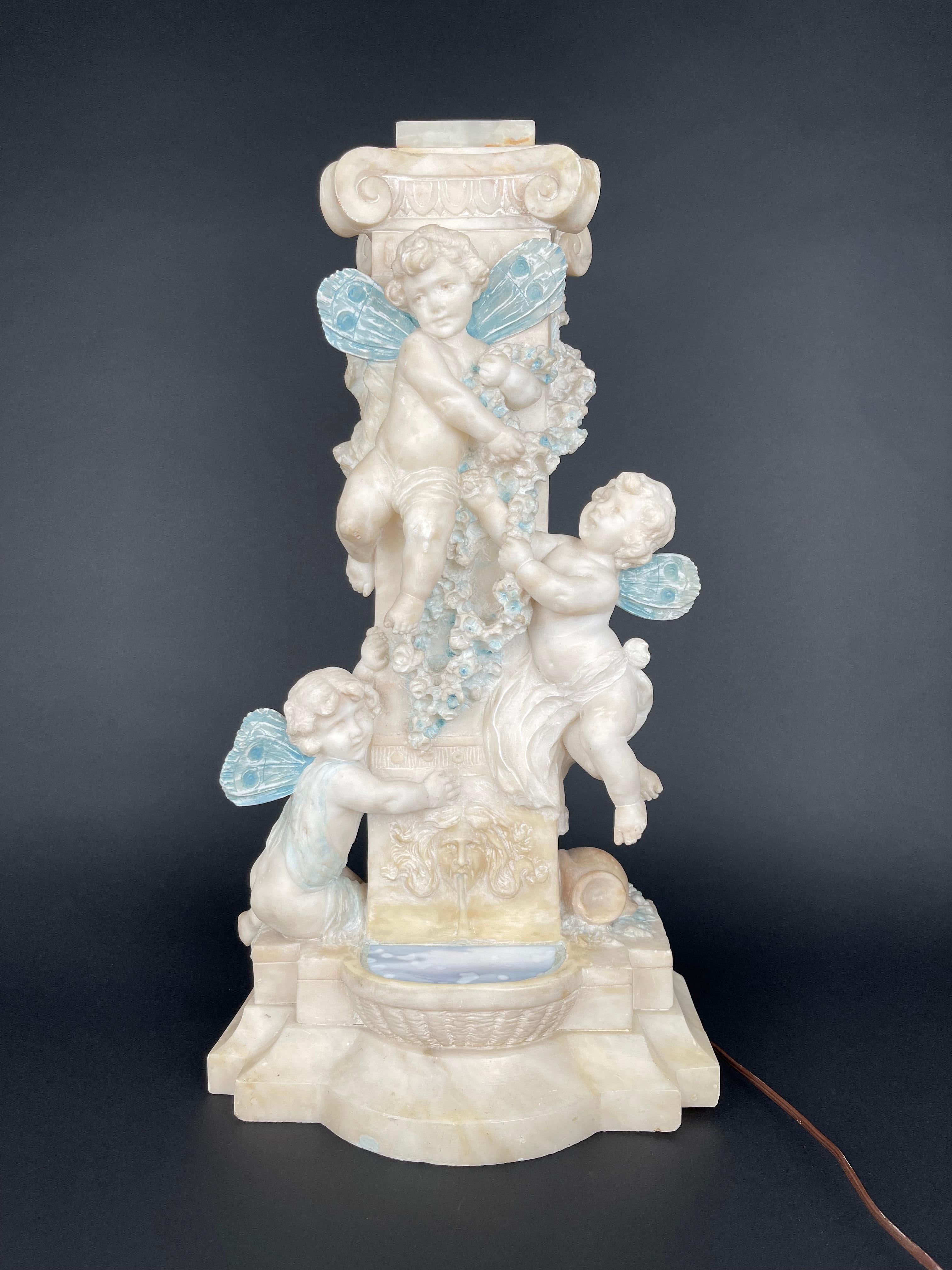 An Art Nouveau Hand Carved Marble Alabaster Figural Lamp. The lamp is finely carved in the shape of a fountain with flying cupid angels holding flowers. Under the cupids is a carved satyr that water comes out of his mouth and flows down to a small