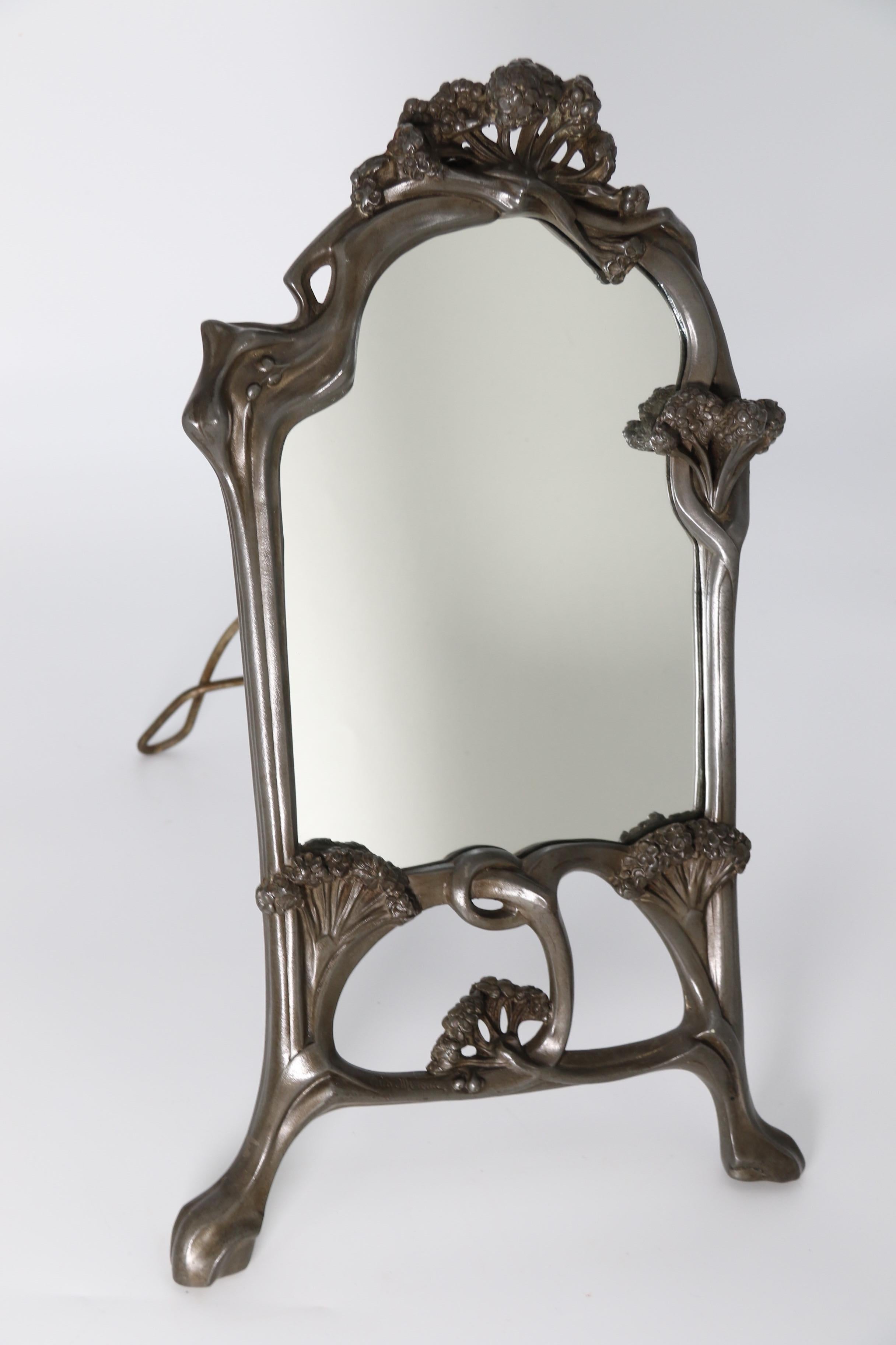 
This stylish and heavily cast solid pewter mirror is a freestanding table mirror with a hinged easel back stand that folds out onto a stop hinge to support the mirror.

The mirror frame is a sculptural work of art. It was designed and produced by
