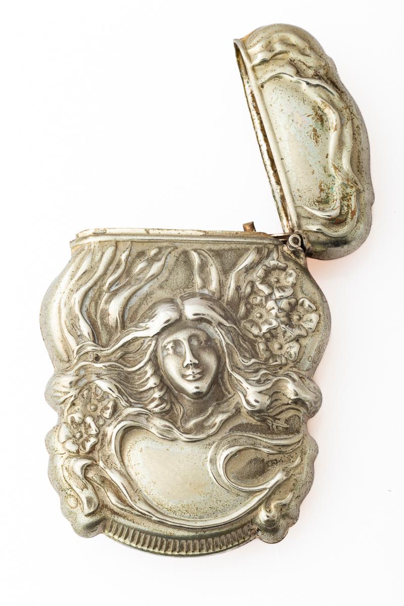 This match safe is made of the finest and most pure sterling silver known as sterline. The front and back are embossed with raised images. On the front is a woman of ideal beauty with long flowing hair that wraps arond the entire face of the
