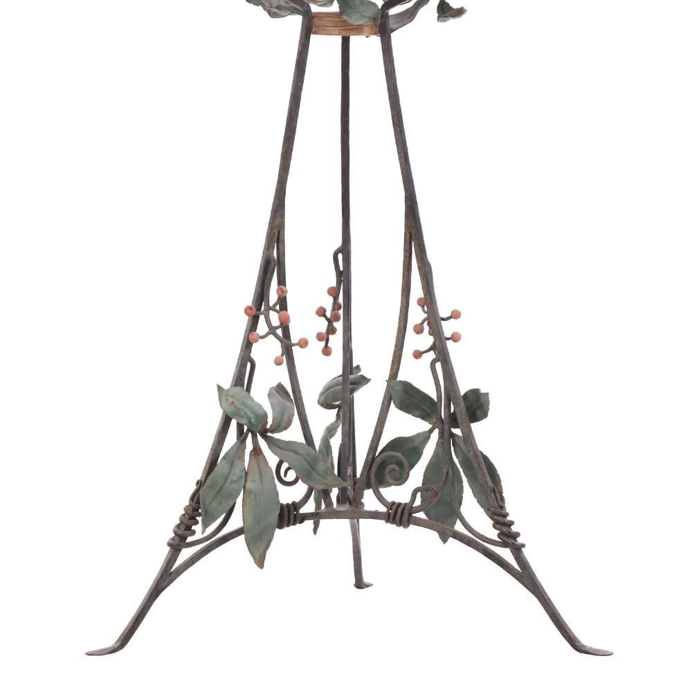 ¡Una encantadora jardinera de hierro de estilo Art Nouveau! Presenta elegantes líneas curvas de alambrismo abierto y detalles decorativos pintados de hojas y bayas en el cuenco superior, apoyado en una base trípode. El diseño fluido capta la