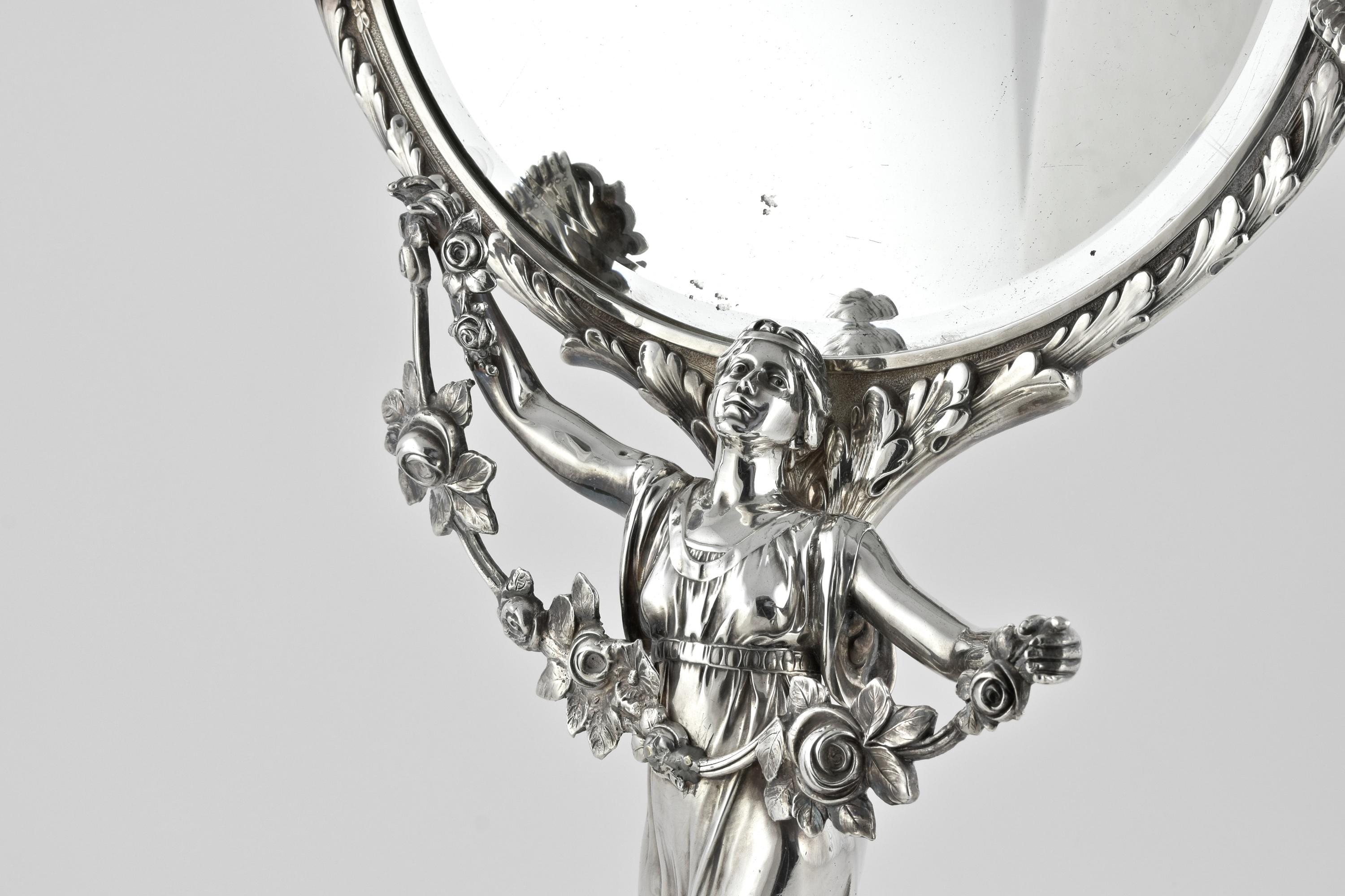 Stunning figural mirrors such as this would have adorned the bedrooms of society ladies throughout the 19th and into the early 20th centuries! The circular base, raised on four feet is boldly engraved with acanthus leaf decoration. The stem formed