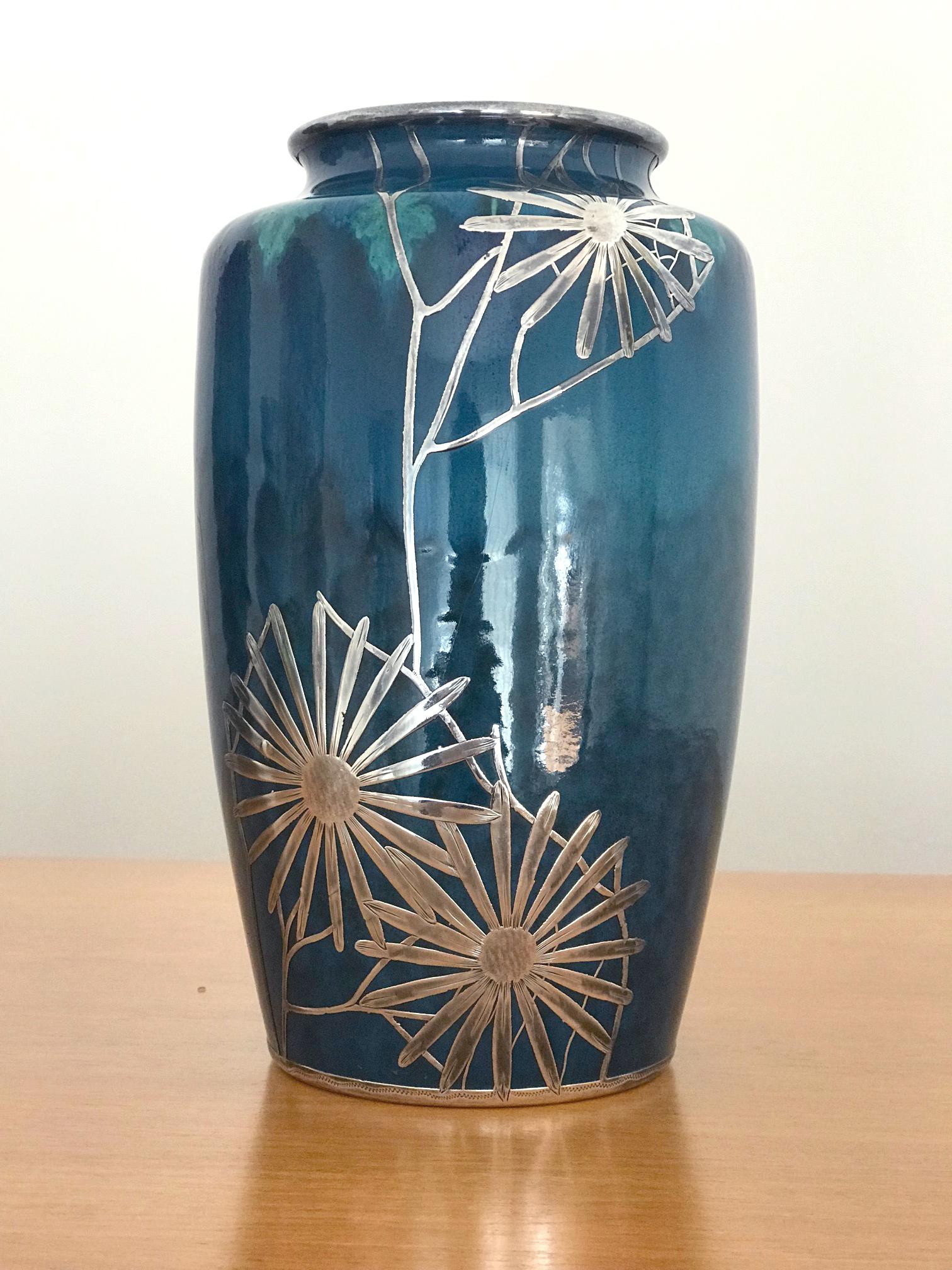On offer here is a porcelain vase of blue glaze with silver overlay circa 1910s in the Art Nouveau style. The peacock blue vase is decorated with a subtle turquoise leaf wreath on the shoulder and marked underneath. The maker is not identified