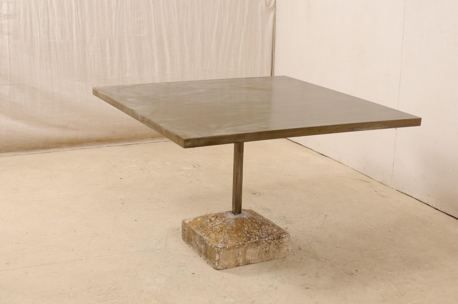 An artisan made custom 4 feet square table with an old Spanish plinth base. This table has been modernly designed in clean lines and features a patinated iron top, square in shape, with a squared iron central column which terminates into an old