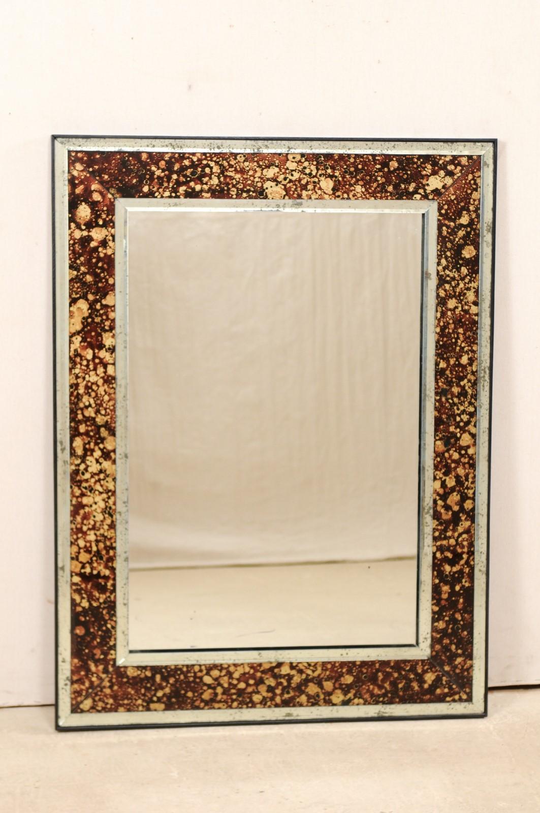 An American artisan made custom mirror with églomisé surround. This rectangular-shaped mirror features a fabulous faux tortoise églomisé surround, brown in color, framed within thinner antiqued mirror moldings. The tortoise coloring is primarily