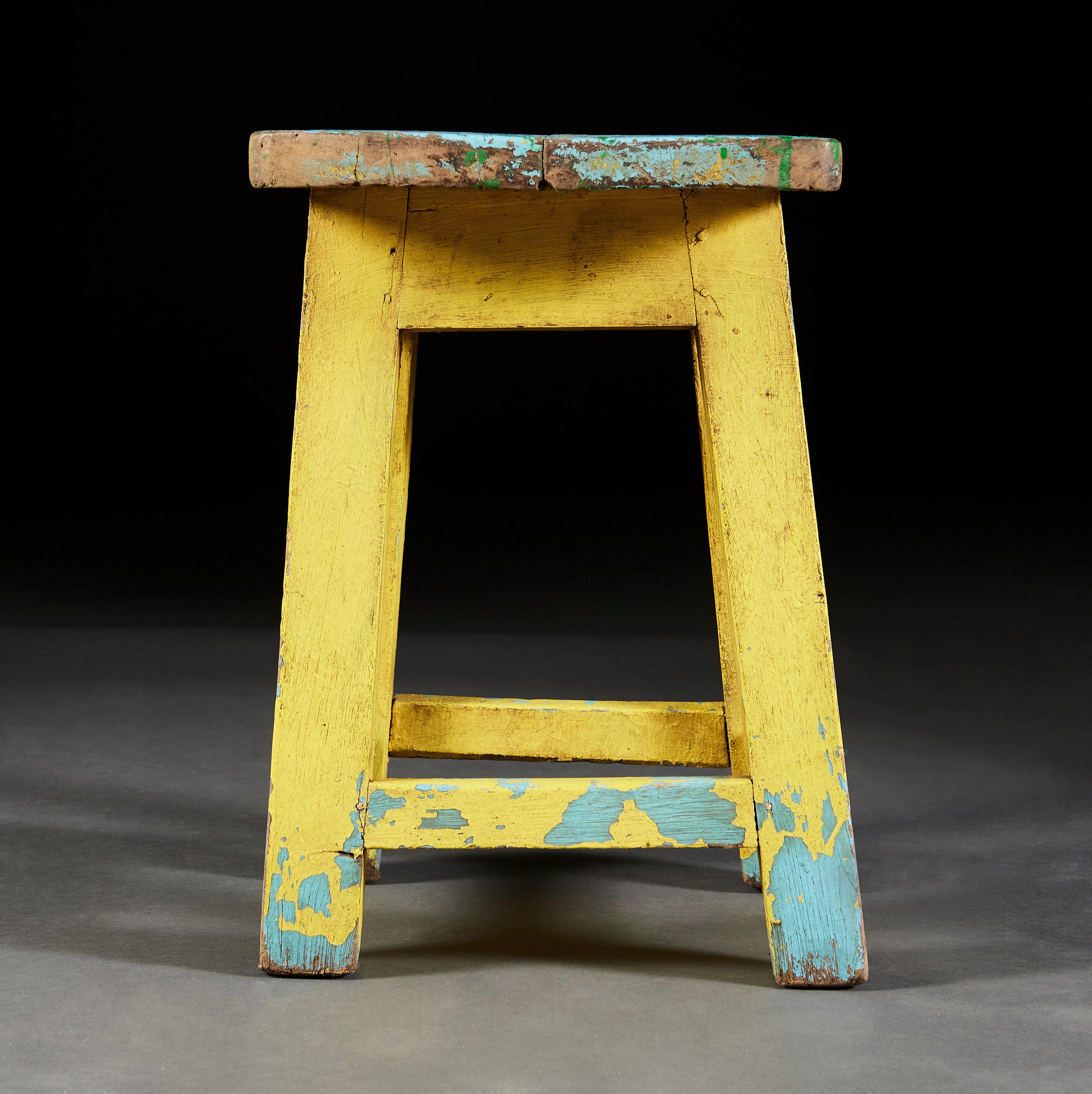 A charming artist’s stool with residual painted surface in yellow, blue and green all supported on four legs joined with a stretcher.