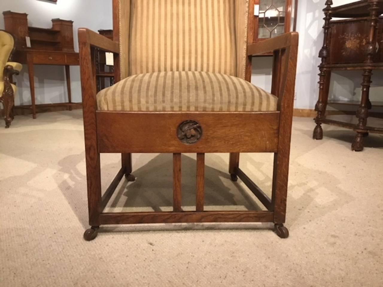 An Arts & Crafts period oak winged armchair possibly by George Montague Ellwood. The winged sides each with finely carved oak leaf and acorn roundels to the shaped upholstered back. Having stylised Arts & Crafts open arms and a sprung seat the whole