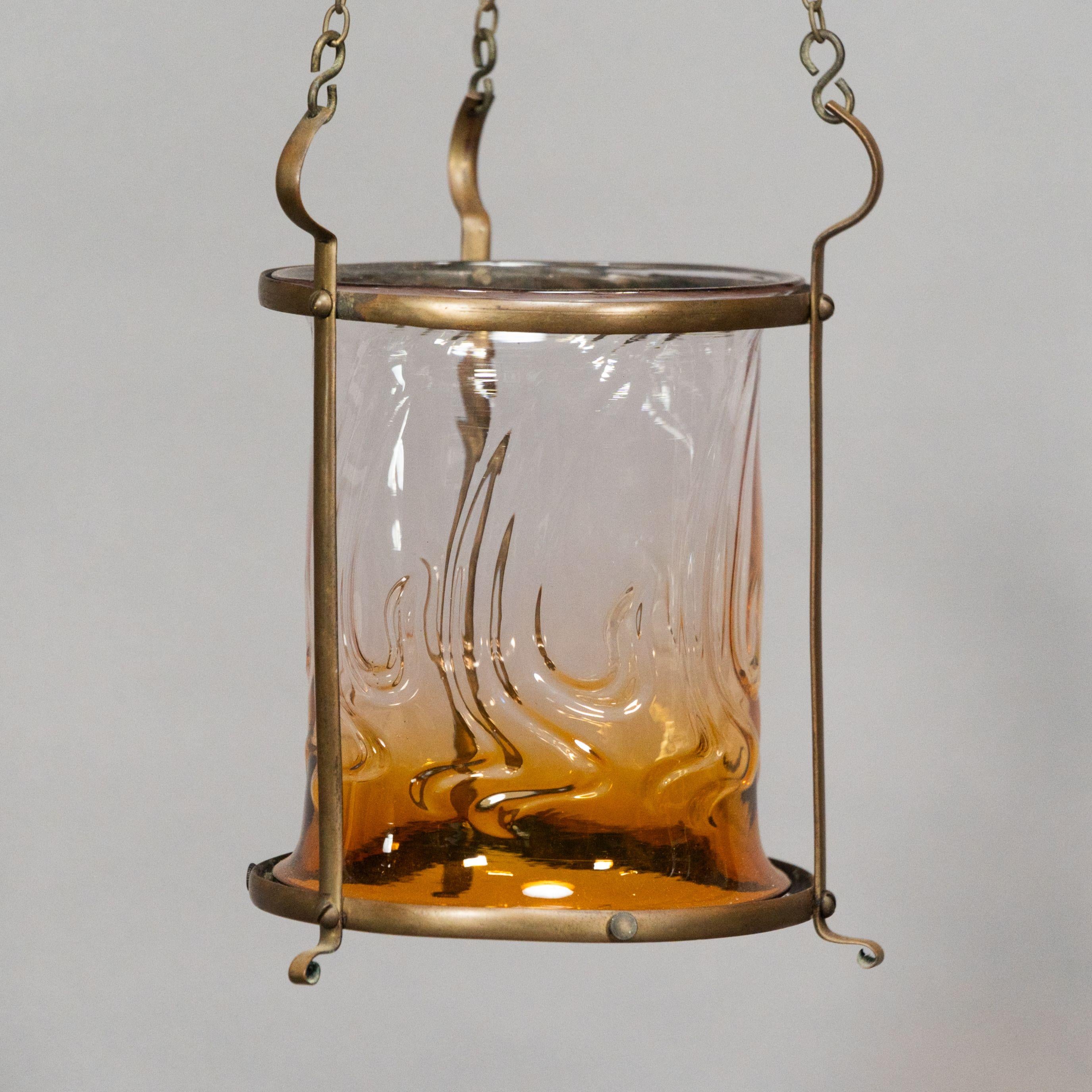 Lanterne en laiton de style Arts and Crafts avec un abat-jour subtilement teinté de bronze et un tourbillon soufflé dans le verre. Hauteur de la lanterne 10, hauteur de la chaîne réglable 15, largeur 8