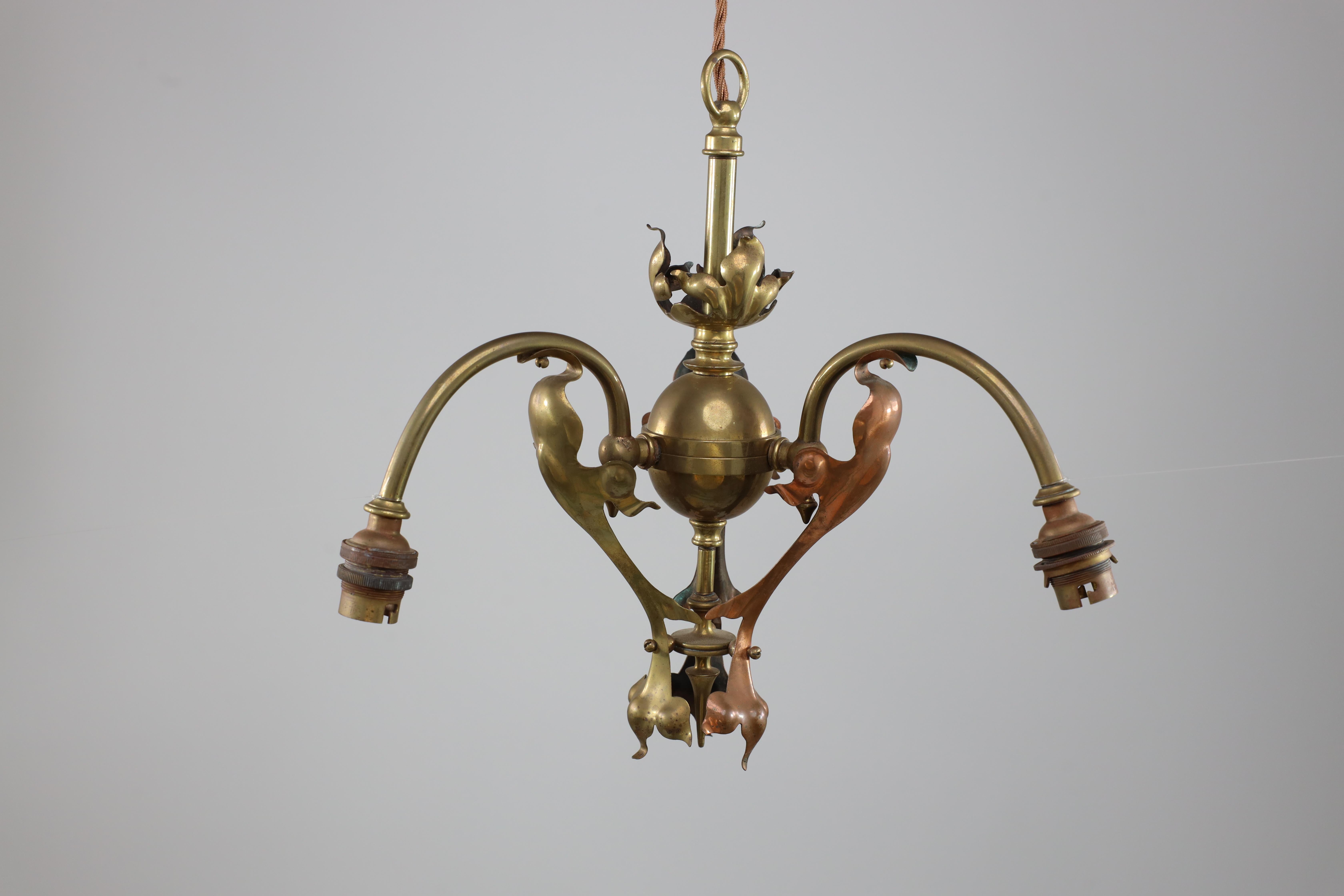 An Arts and Crafts brass three arm ceiling light with a flower bud to the top and pierced leaf decoration to the arms. We have original brass chain to hang this at any height.