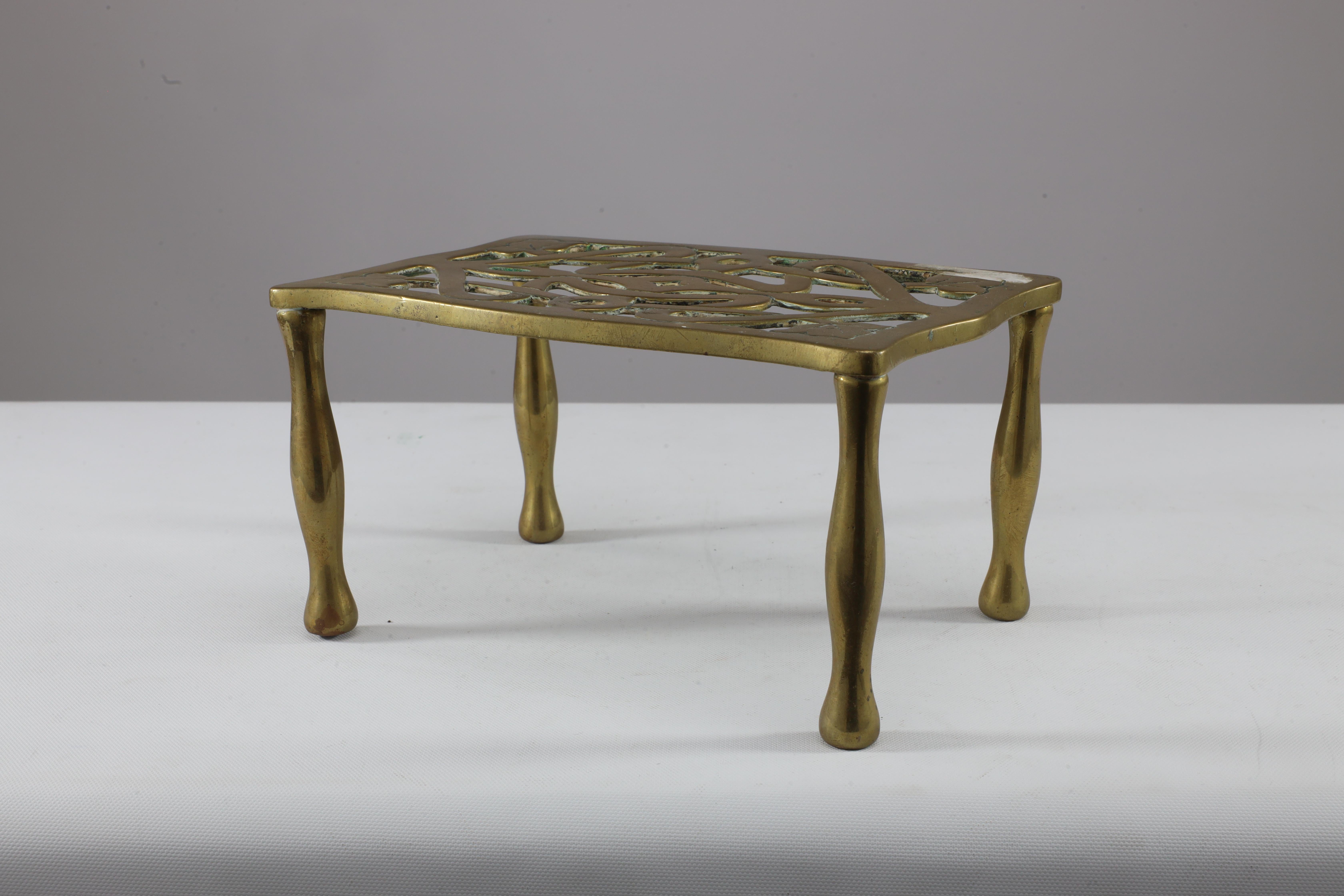 An Arts and Crafts brass trivet with pierced floral decoration to the top, on shaped legs.