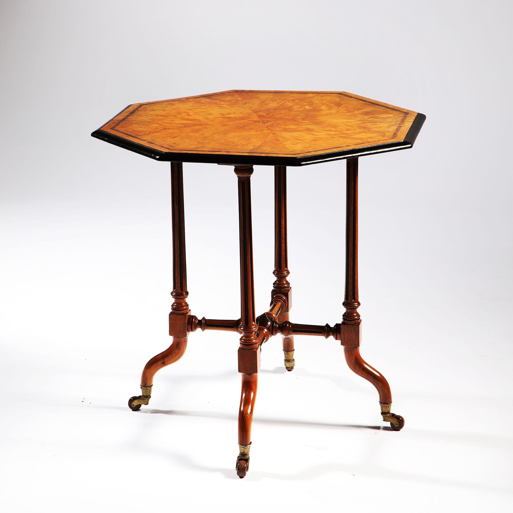 An Arts & Crafts burr walnut occasional table, the octagonal top resting on four legs with a turned X-form stretcher, the legs terminating in brass castors. Stamped to the underside with ivorine plaque ROUGH & SONS.

 