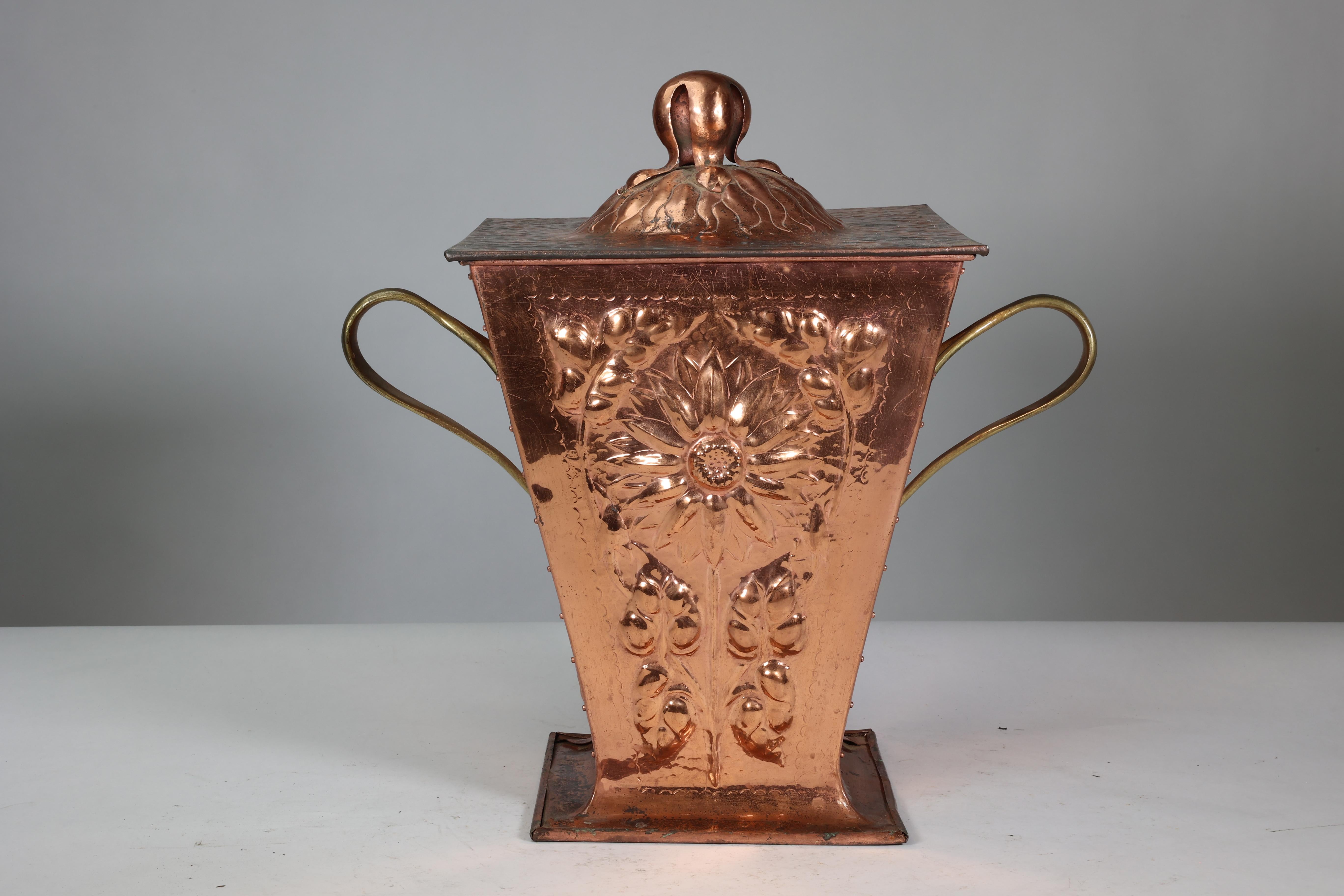 An Arts and Crafts copper coal bucket and lid with a sunflower seed pod handle, and hand-hammered sunflowers to all four sides each framed with subtle half-moon chasing. With cold copper riveting to the four corners and sinuous organic brass handles