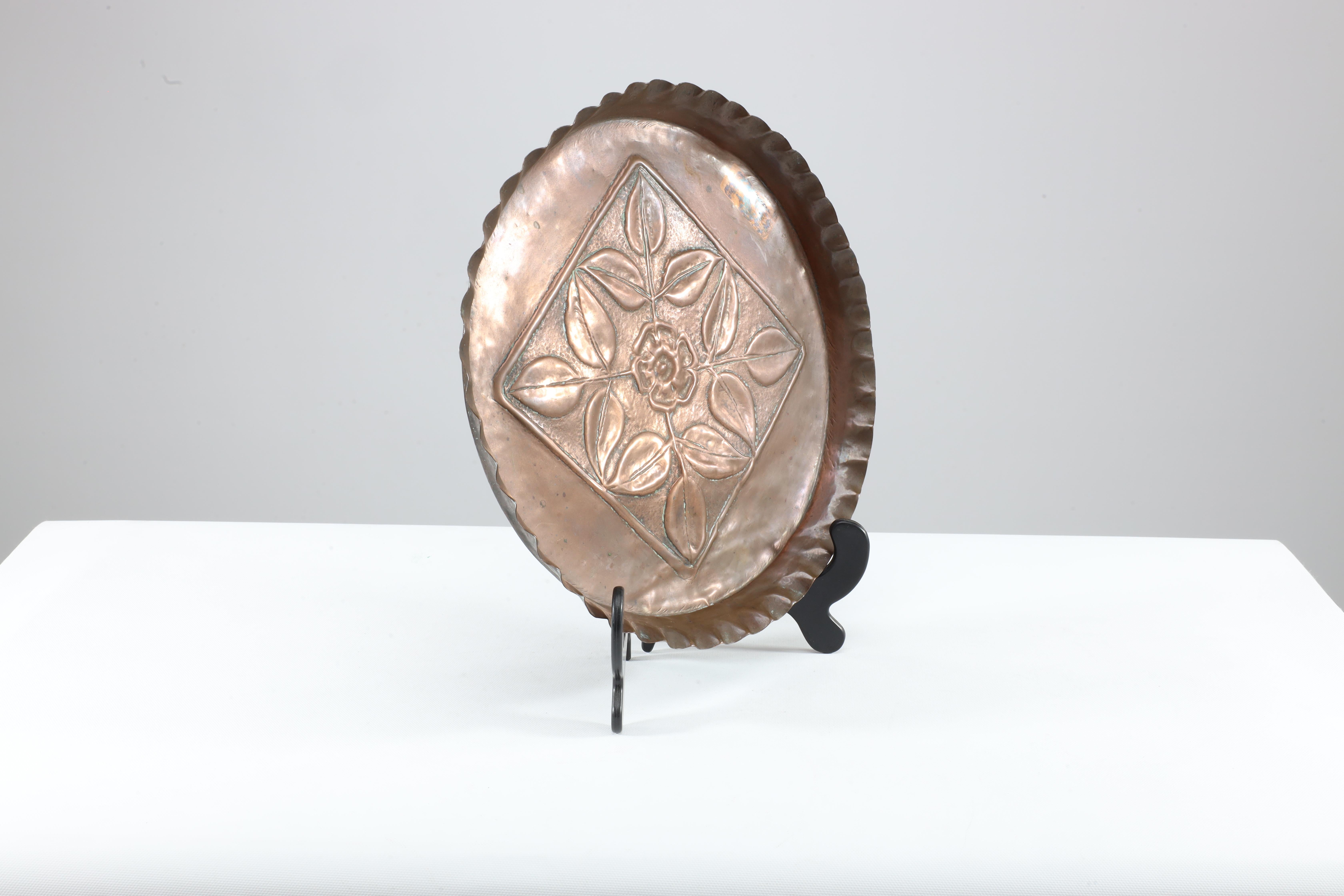 Ein Kupferteller aus der Zeit des Arts and Crafts mit einem Tortenrand und Blumendekoration in der Mitte.