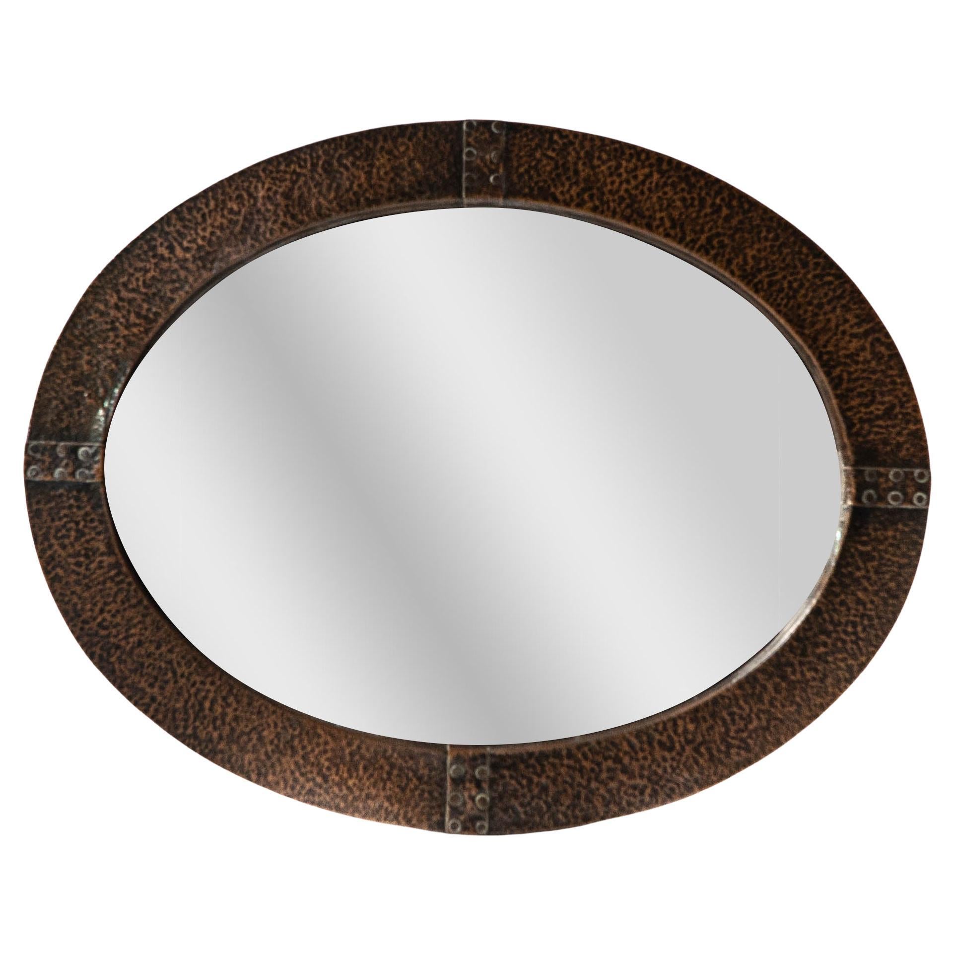 An Arts and Crafts hand hammered copper oval mirror with riveted straps