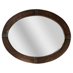 An Arts and Crafts hand hammered copper oval mirror with riveted straps