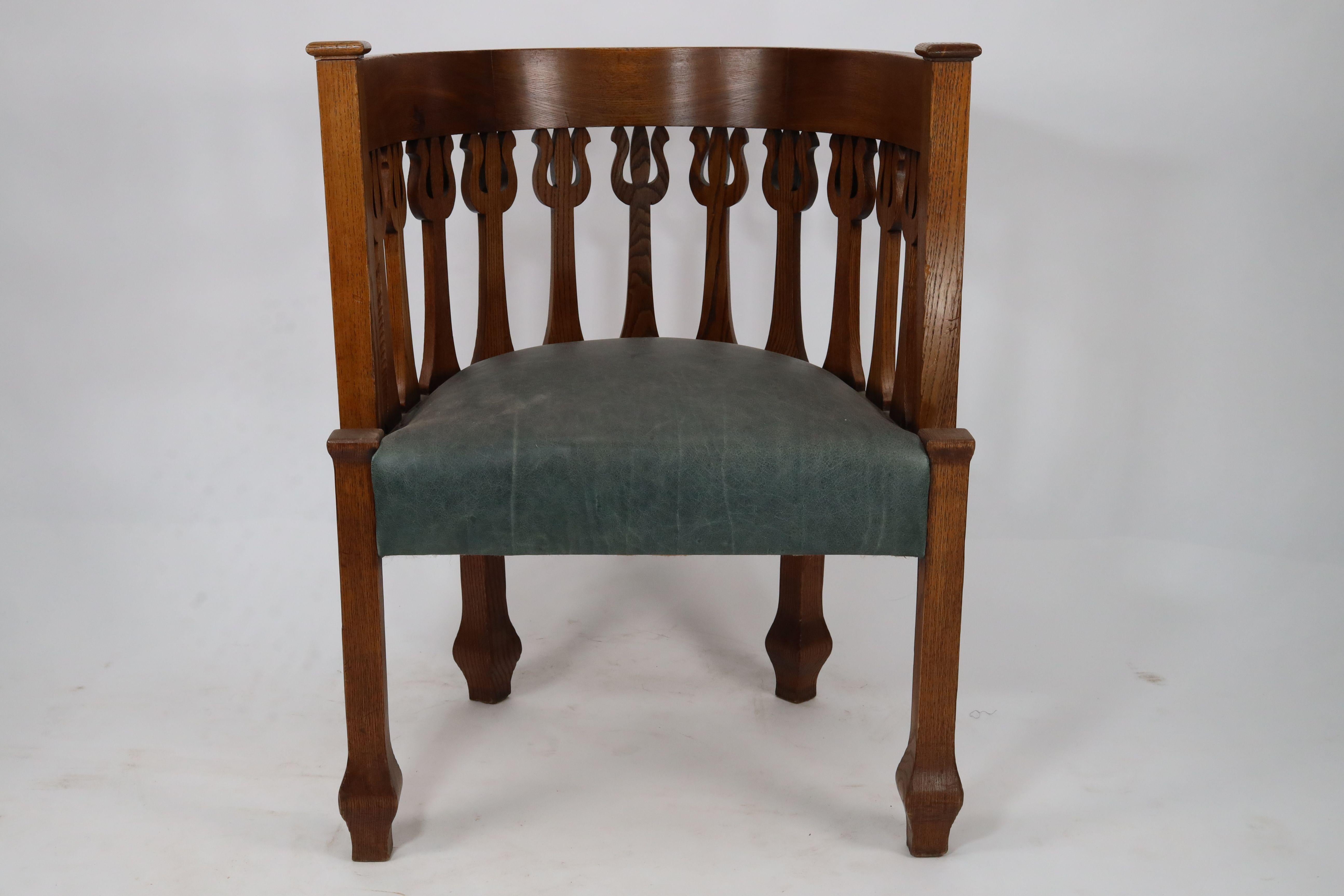 An Arts and Crafts oak armchair with stylized floral upright decoration to the curvaceous back, the comfy seat has been professionally re-upholstered in quality green hide that will last a lifetime of bum polishing. Stood on square legs with carved