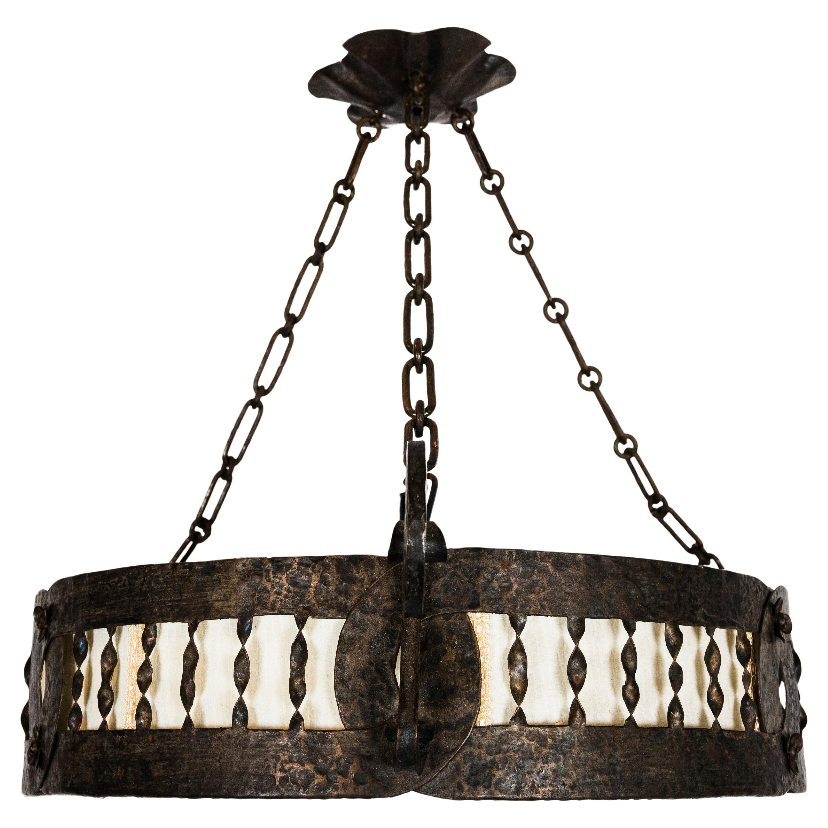 A Northern European Arts and Crafts pendant light. With a hammered and patinated brass frame, and a fabric covered insert. Contains three medium sockets. Circa 1910
