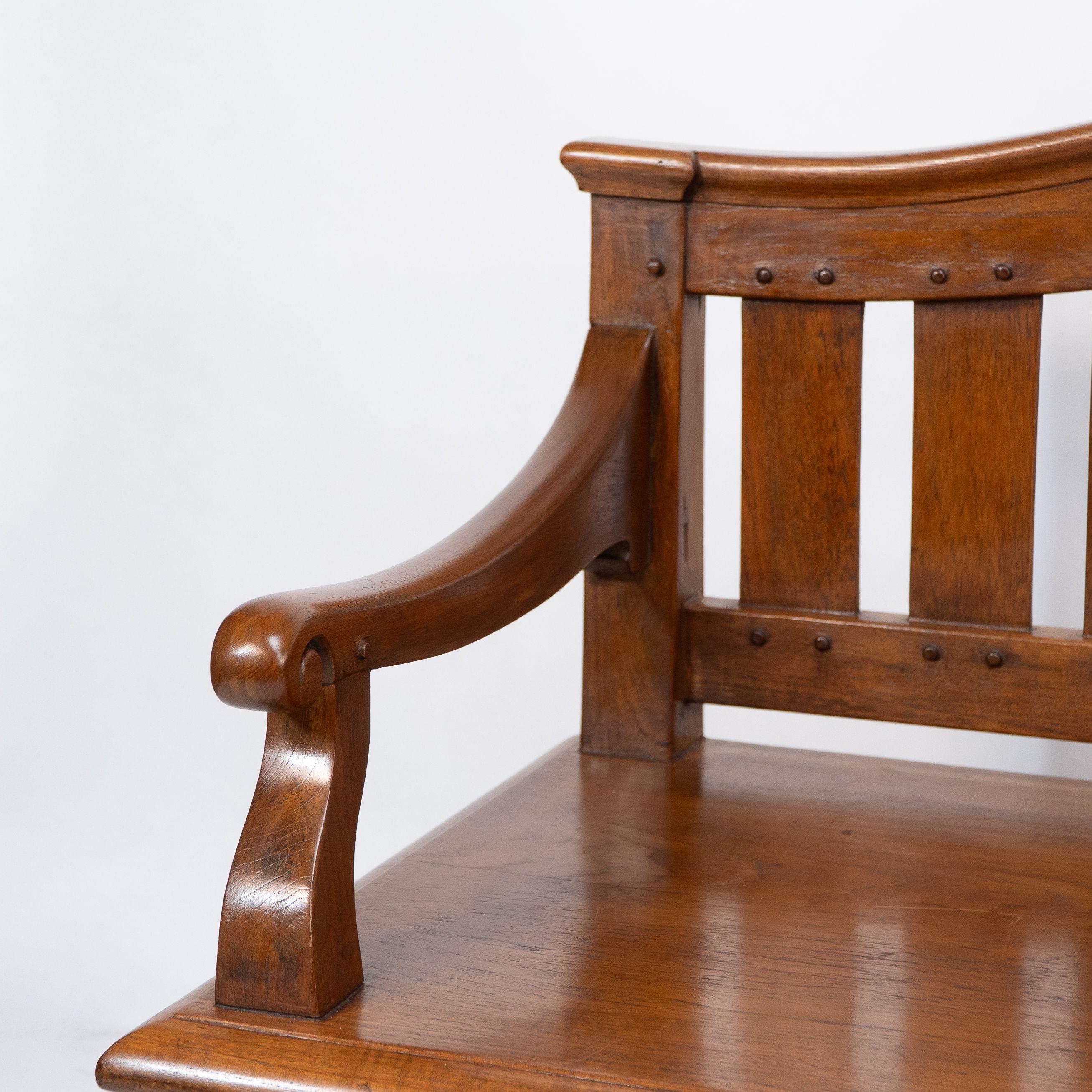 An Arts and Crafts super quality teak hall bench in the style of Arthur Simpson with a flowing heart shaped design to the back and a moulded head rail, scroll hand carved arms, and decorative exposed double pegged joints throughout. A moulded edge
