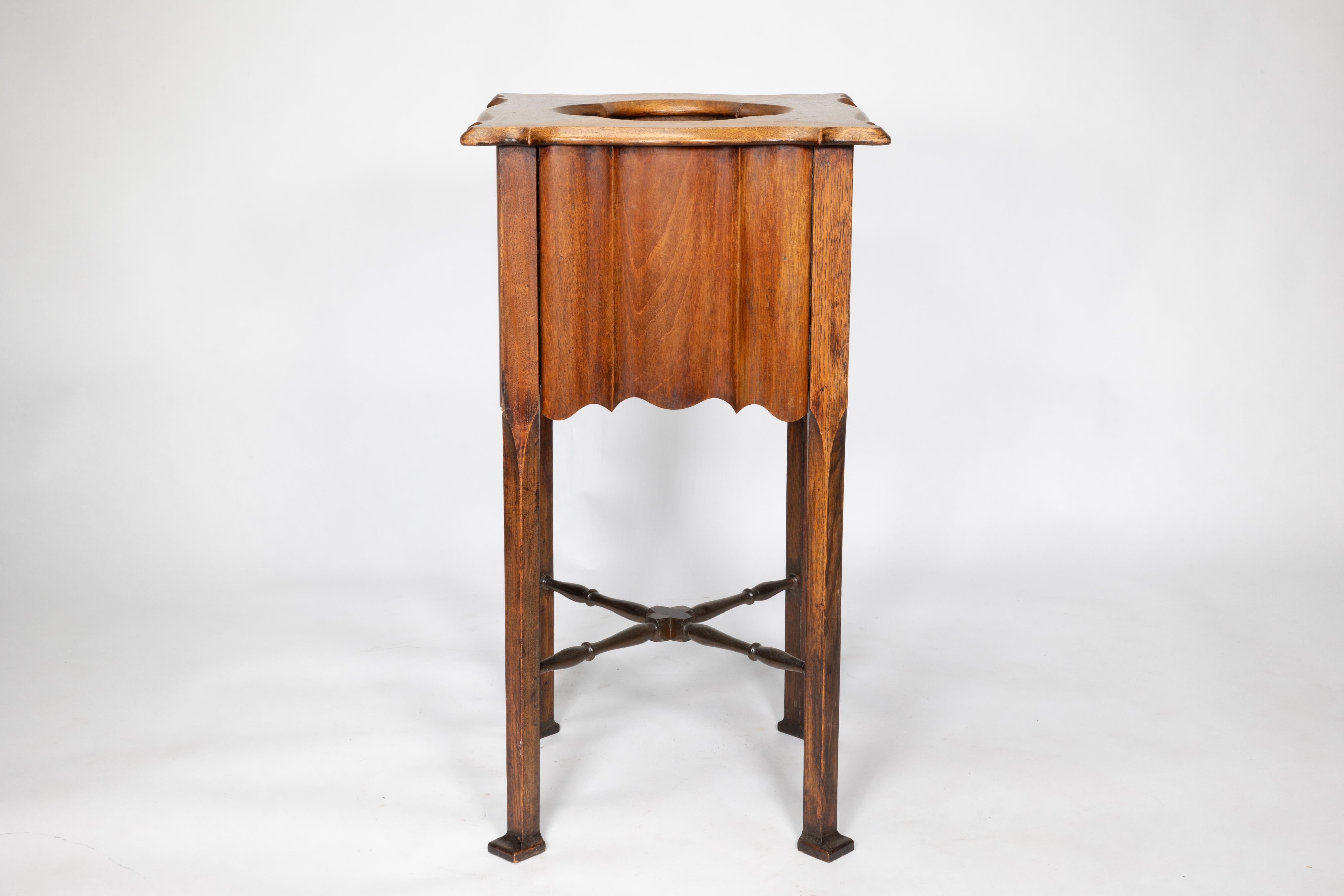Un portapiante in noce Arts and Crafts con piano sagomato e lati in stile scanalato su gambe dritte e smussate unite da una traversa.