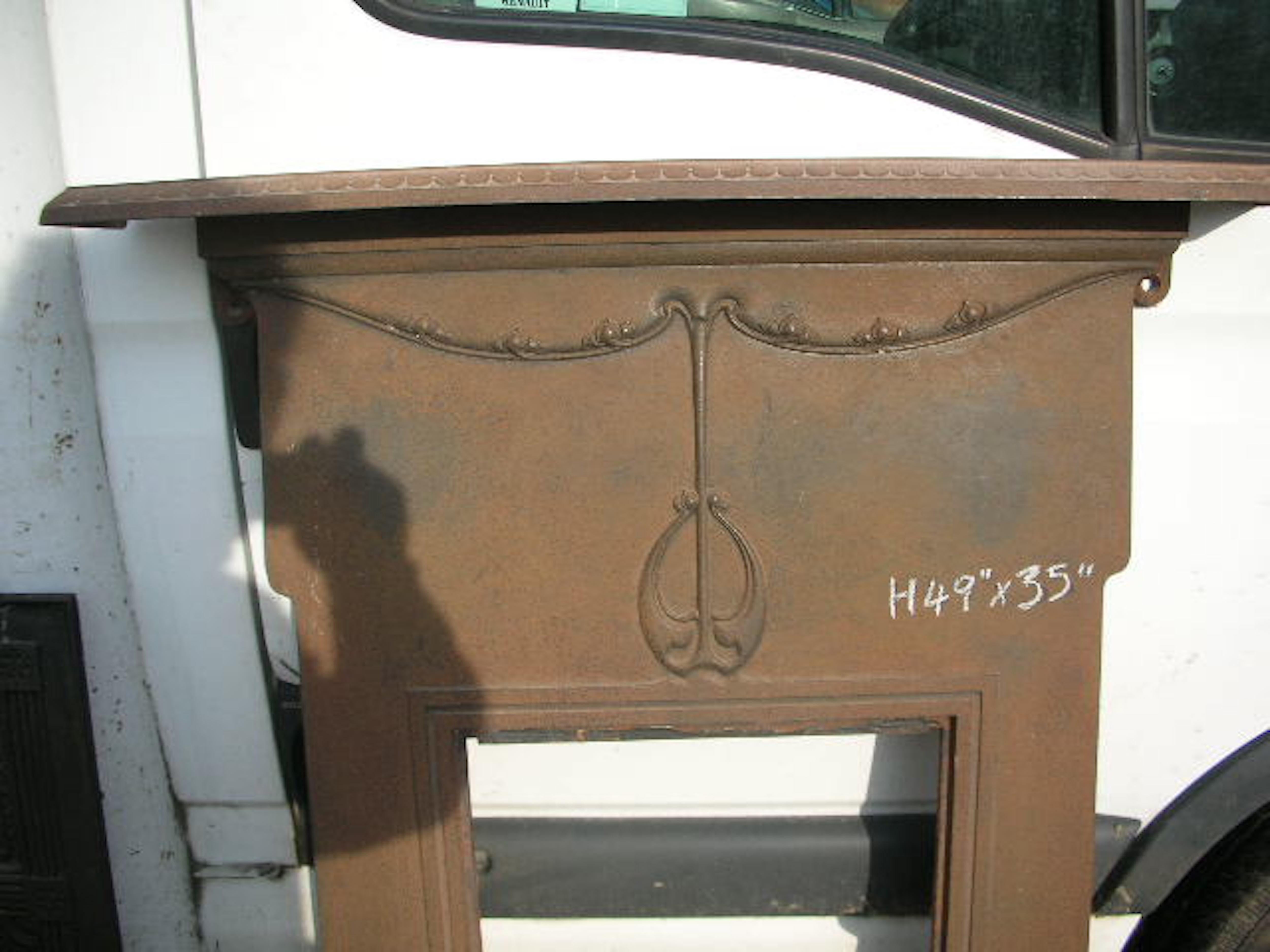 An Arts and Crafts / Art Nouveau period cast iron fireplace, the mantle with scalloped details to the edges. The main body with a central upper stylized floral seed pod detail, growing up and flowing to each side with sweet little three leaf