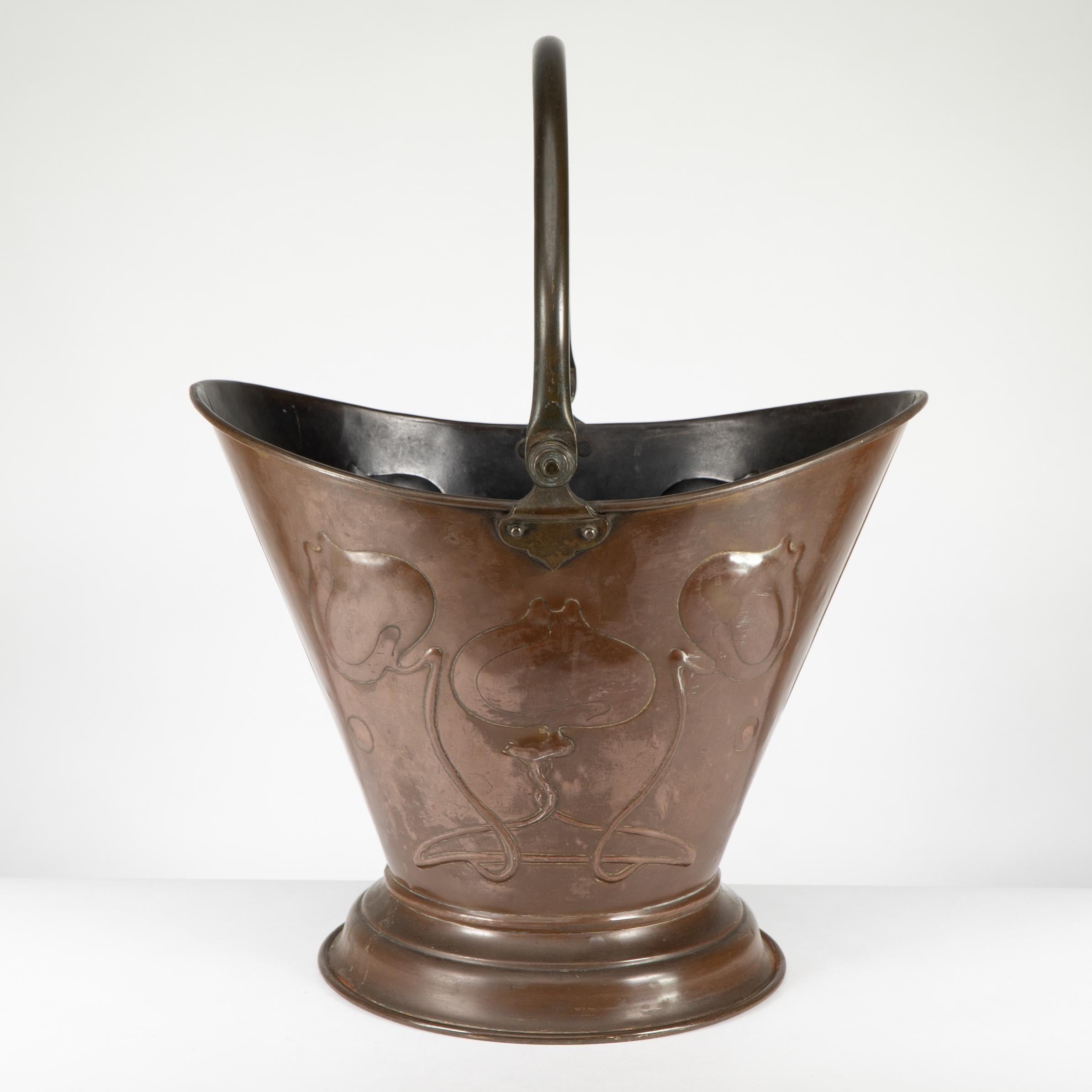 Seau à charbon en cuivre de style Arts and Crafts, doté d'une poignée pivotante et d'une décoration florale repoussée sur les côtés, qui conserve une patine chaude non polie de couleur chocolat.