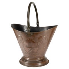 An Arts & Crafts copper coal bucket with floral decoration and chocolate patina