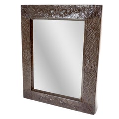 An Arts & Crafts copper mirror with stylized decoration and flower heads