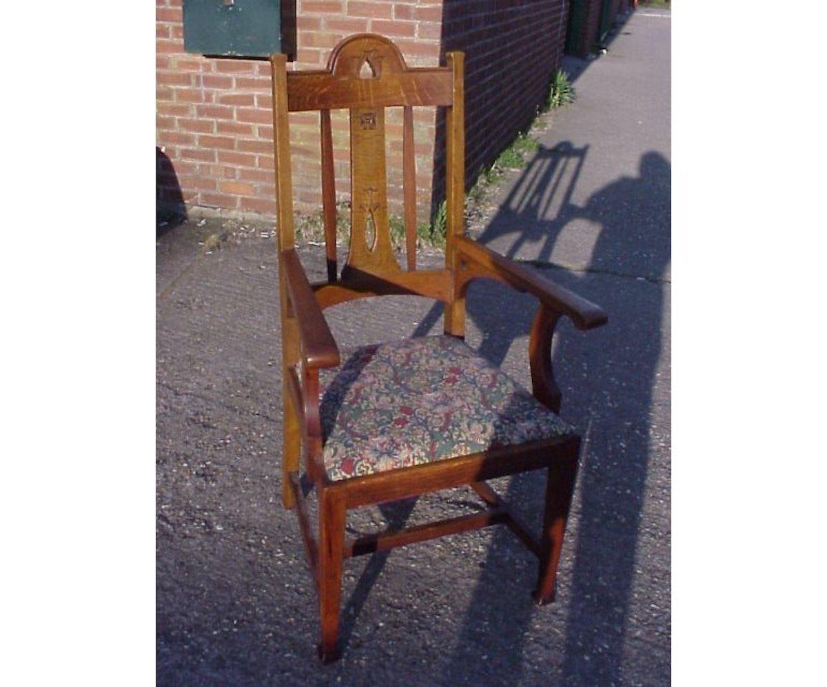 An excellent quality Arts & Crafts oak armchair made by Goodall, Lambs and Heighway of Manchester (stamped under seat rail). With central stylized carved back and pierced sweeping arm supports on square tapering legs, re upholstered in a Morris and