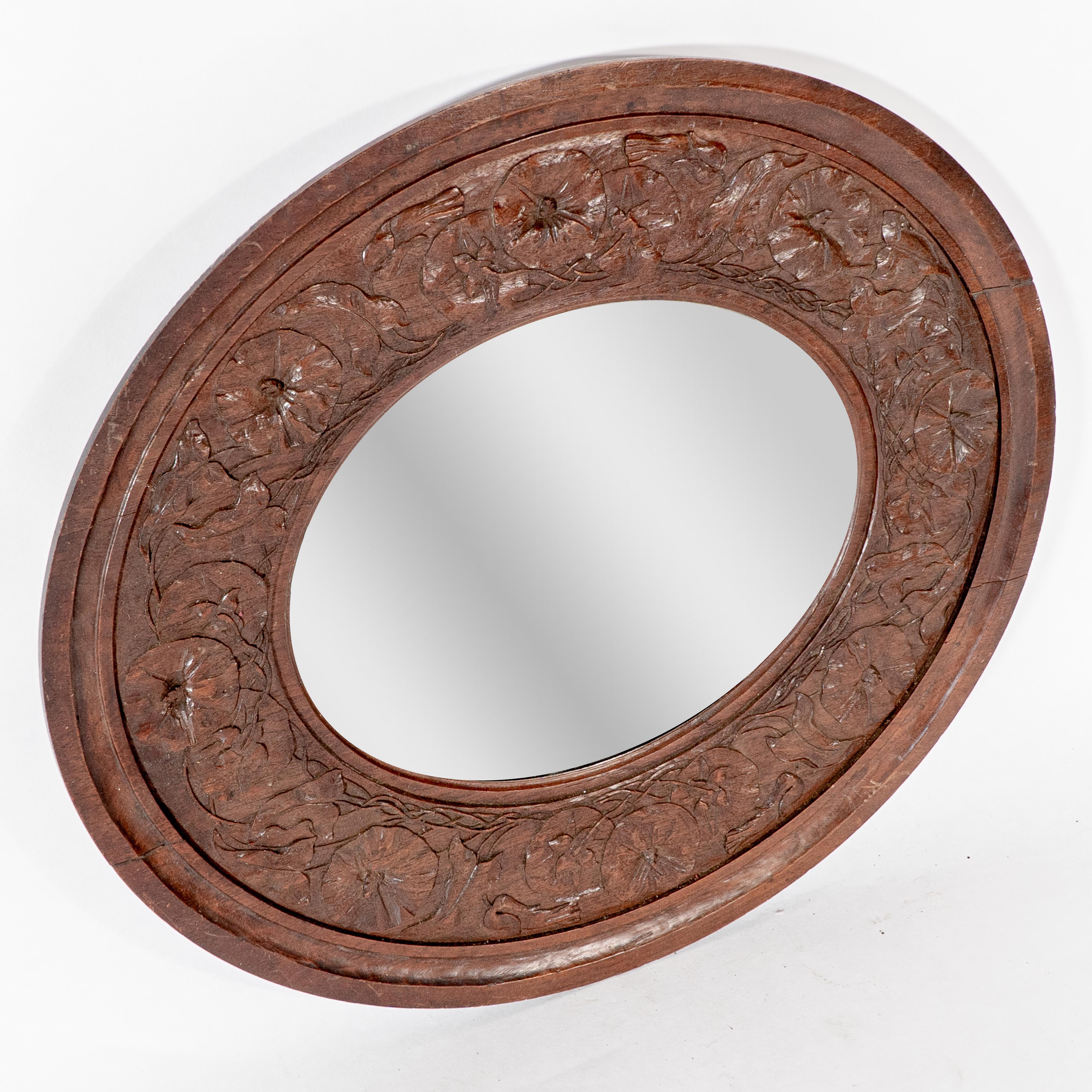 An Arts and Crafts walnut circular mirror with stylized Morning Glory floral carved decoration