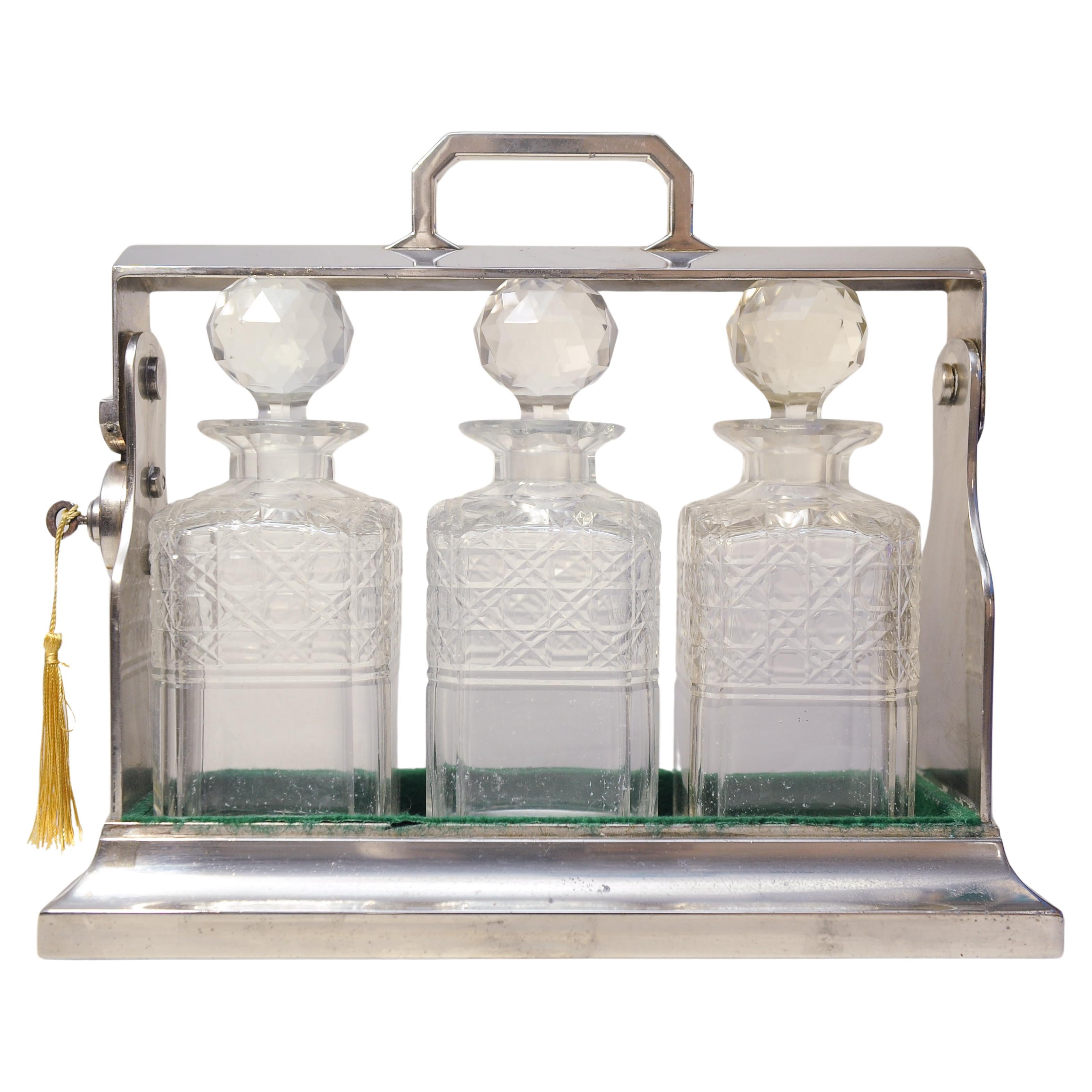 Un Tantalus placcato in argento Art Decor con tre decanter in vetro tagliato Baize foderato con una chiave di lavoro decorativa e una targhetta d'oro.

Realizzato negli anni '20 nello stile di Betjemann con piano regolabile a cerniera.

I