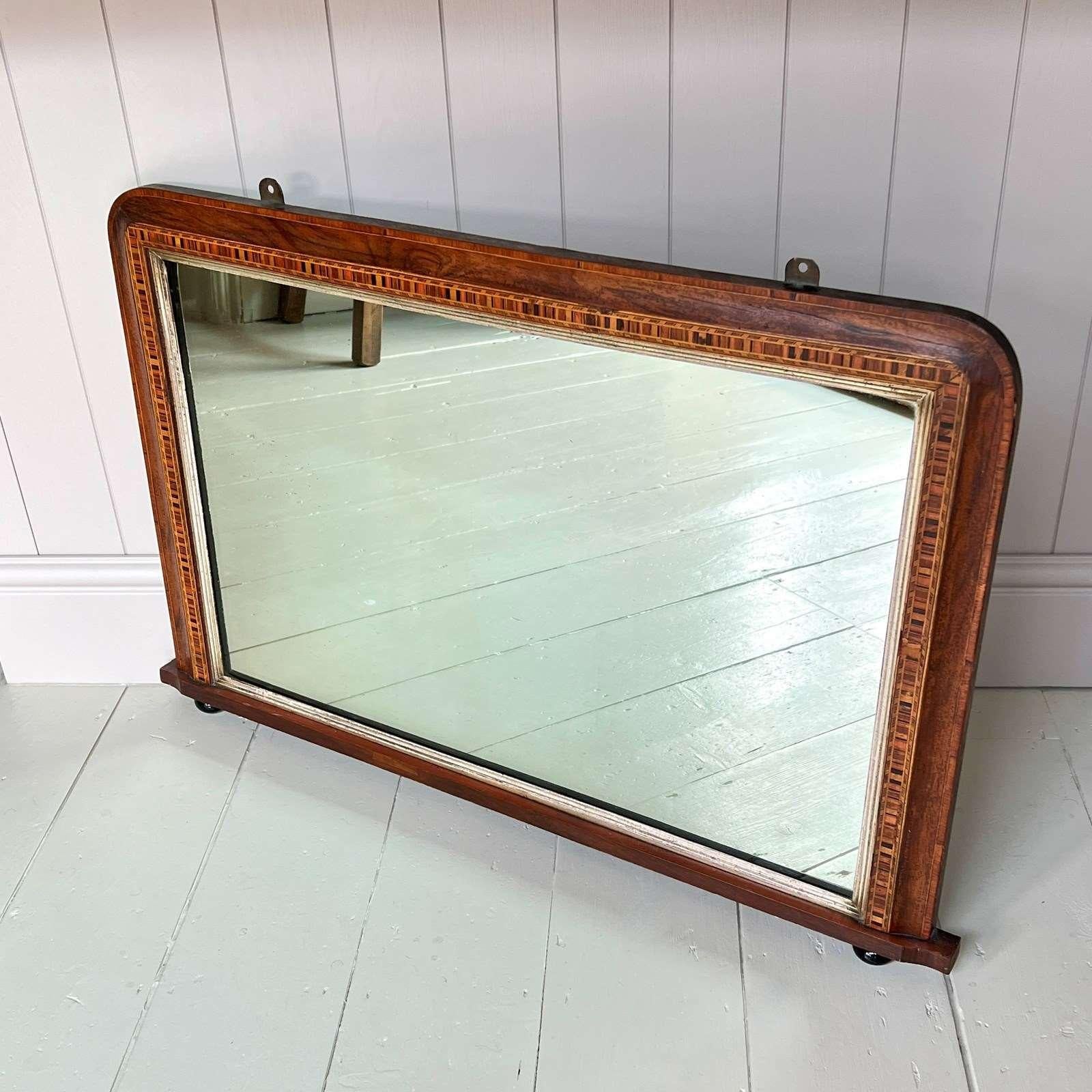 An Edwardian Inlaid Overmantel Mirror. The rectangular mahogany cushion frame with attractive parquetry inlay. Nice contrasting silver gilt slip moulding to the inside of the frame. Standing on black ceramic feet. Wear commensurate with age. One