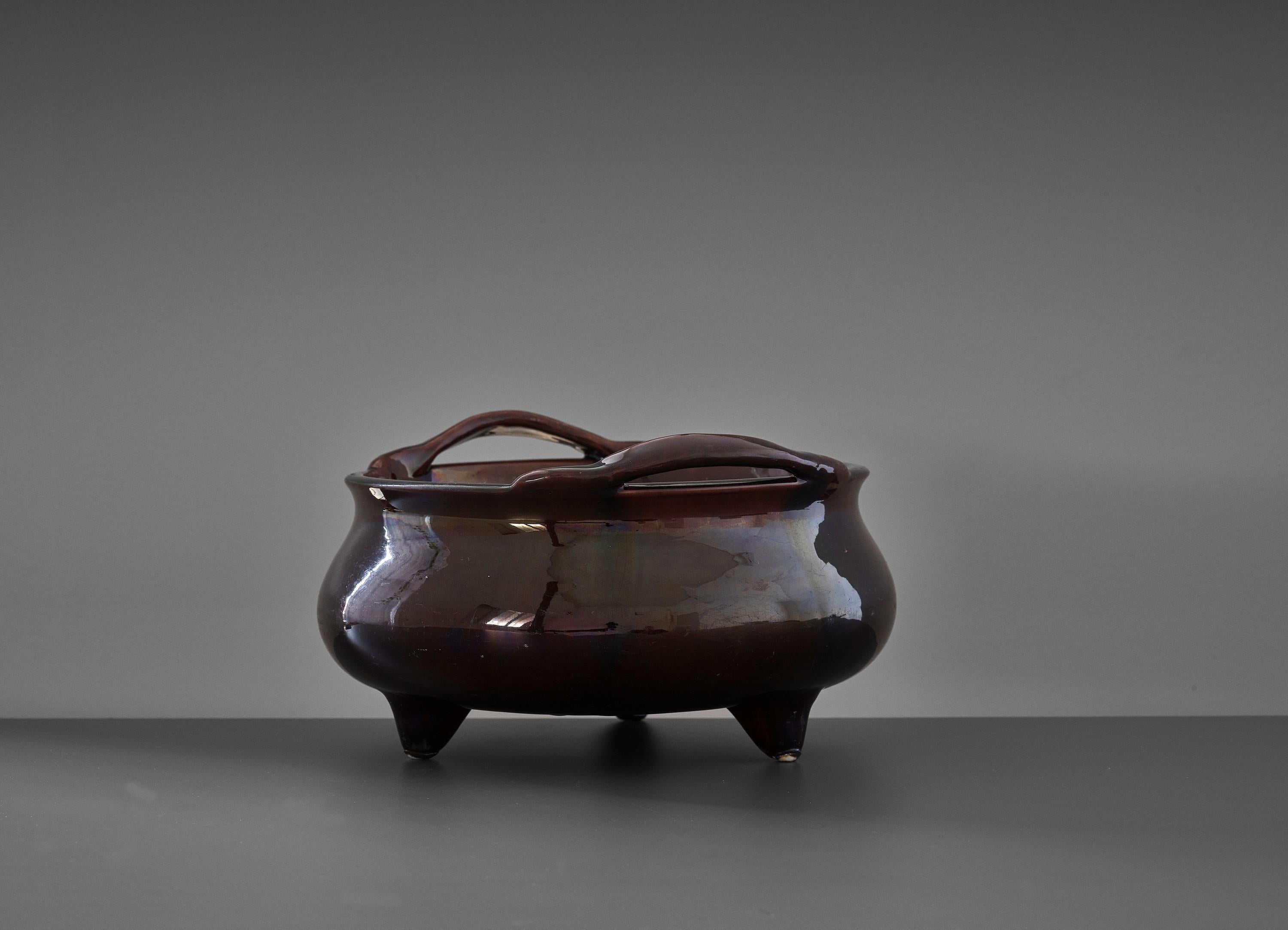 An aubergine-glazed 'Bombe' tripod censer, China, Qing Dynasty, 18th to early 19th century

The compressed globular body supported on three tapered feet, the lipped rim raised on a waisted neck and set with two loop handles, covered overall in a