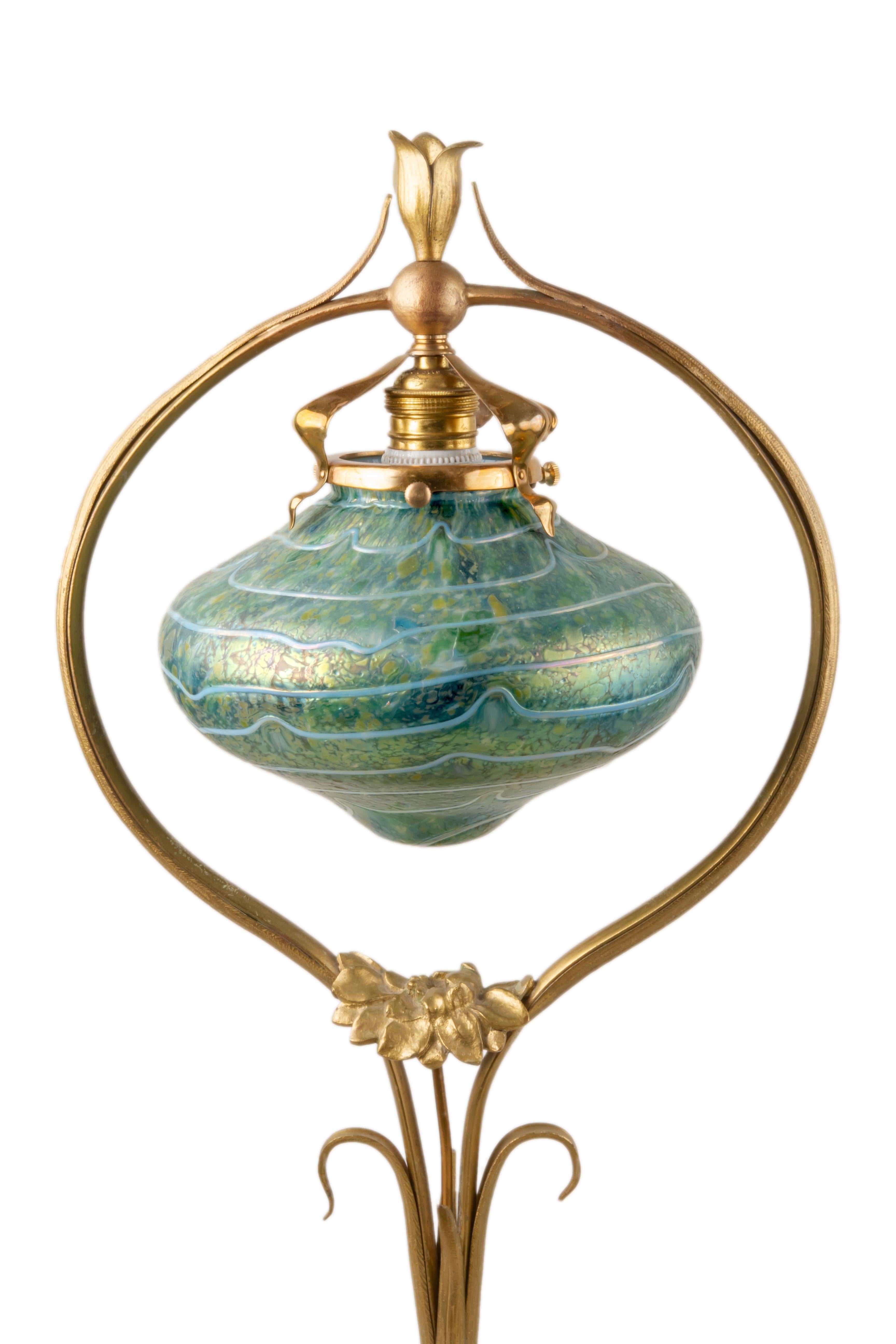 An Austrian Art Nouveau cast bronze and glass decorated Sunflower Desk Lamp decorated with a blue 
 iridescent decorated shade with white applied decoration with in a cast and gilt bronze sunflower decorated lamp base. The shade when illuminated is