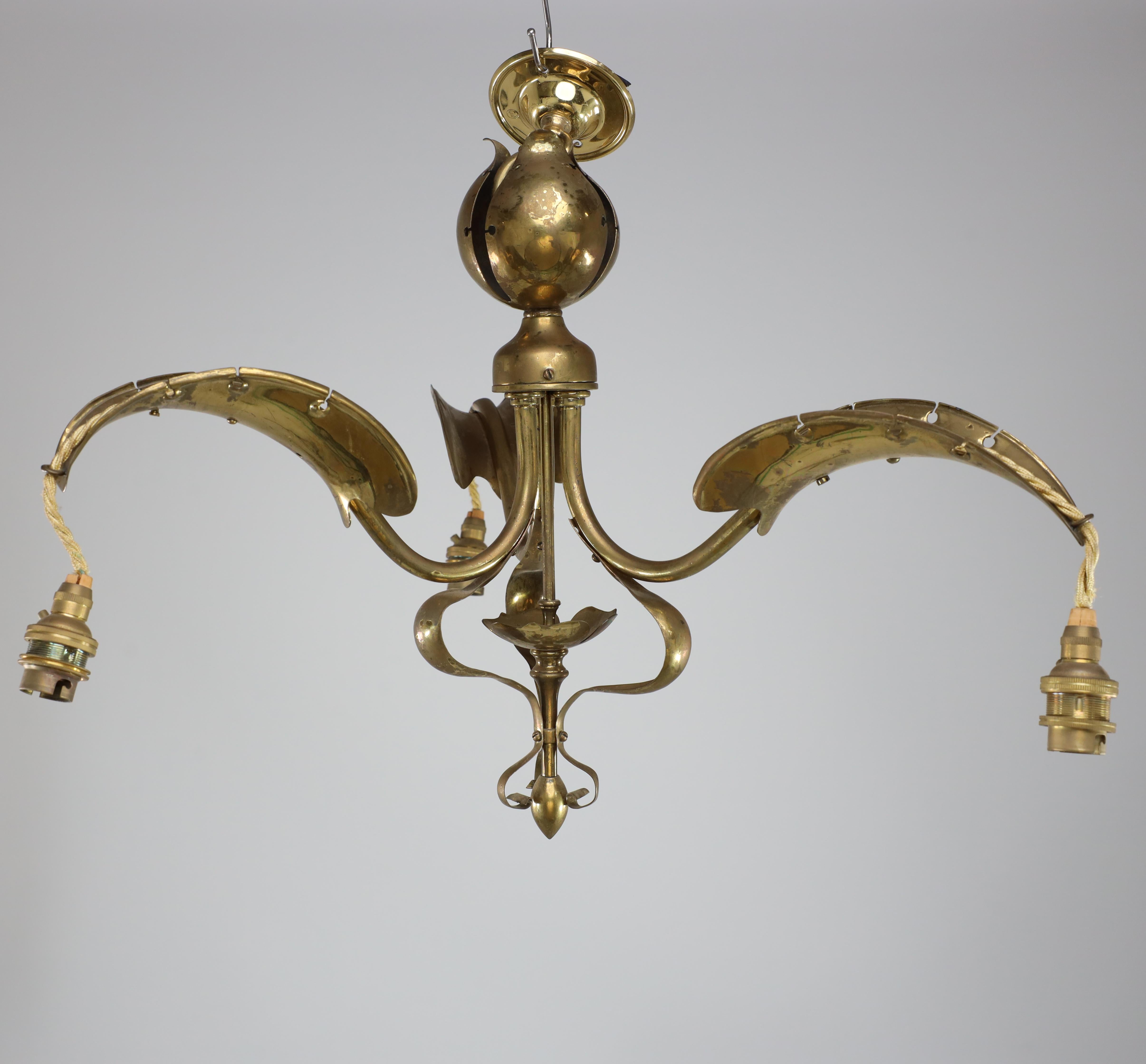 An Arts and Crafts brass three-arm ceiling light with a central shaped sphere and leaf decoration to the arms that follow down to the bottom. We have an original brass chain to hang this at any height.