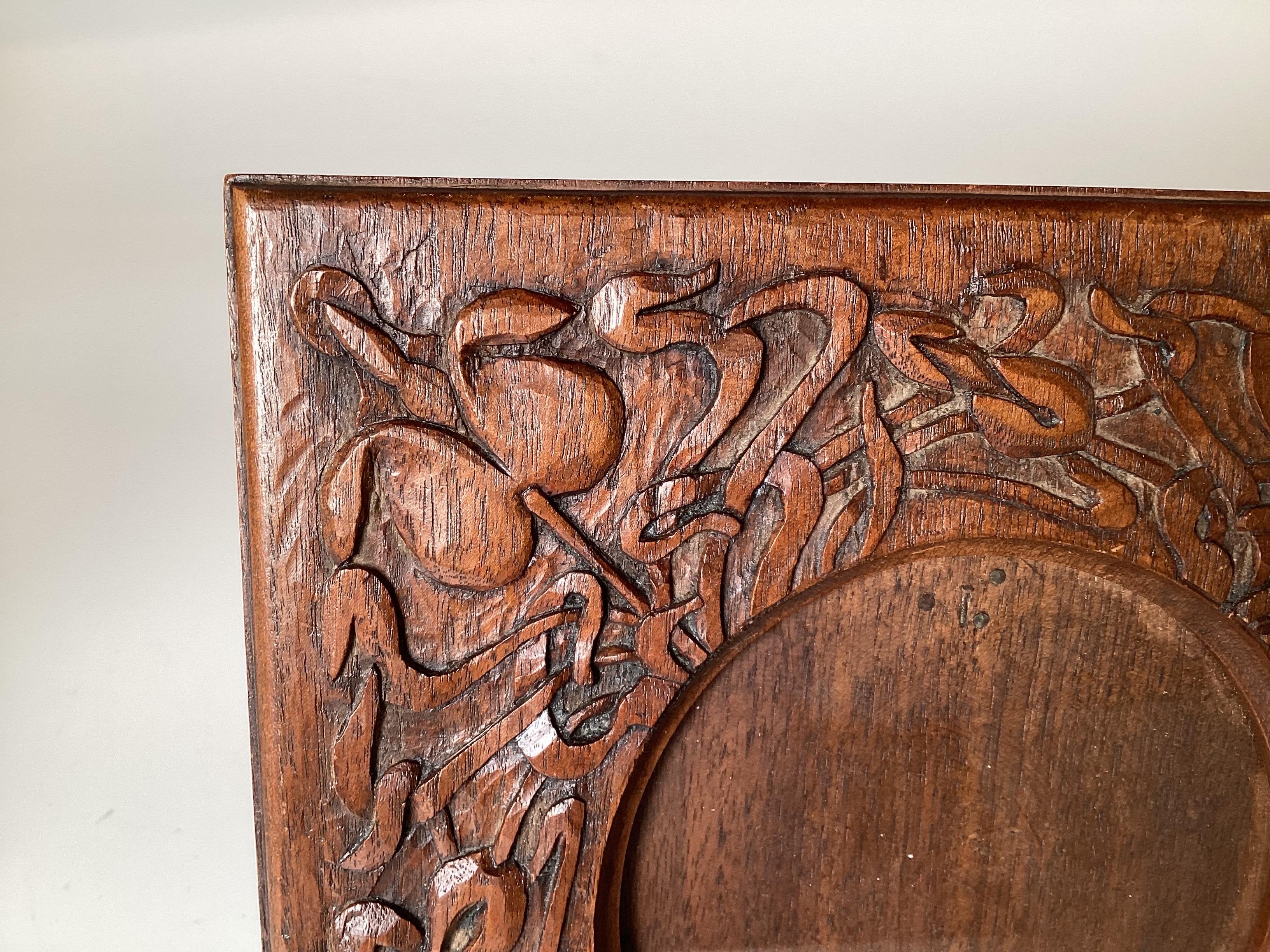 A beautifully hand carved arts and crafts wooden picture frame.  The carved front with organic arts and crafts design with a round opening for picture display.  The back is an easel style.  8 inches high, 7.75 inches wide. There is a hard to read