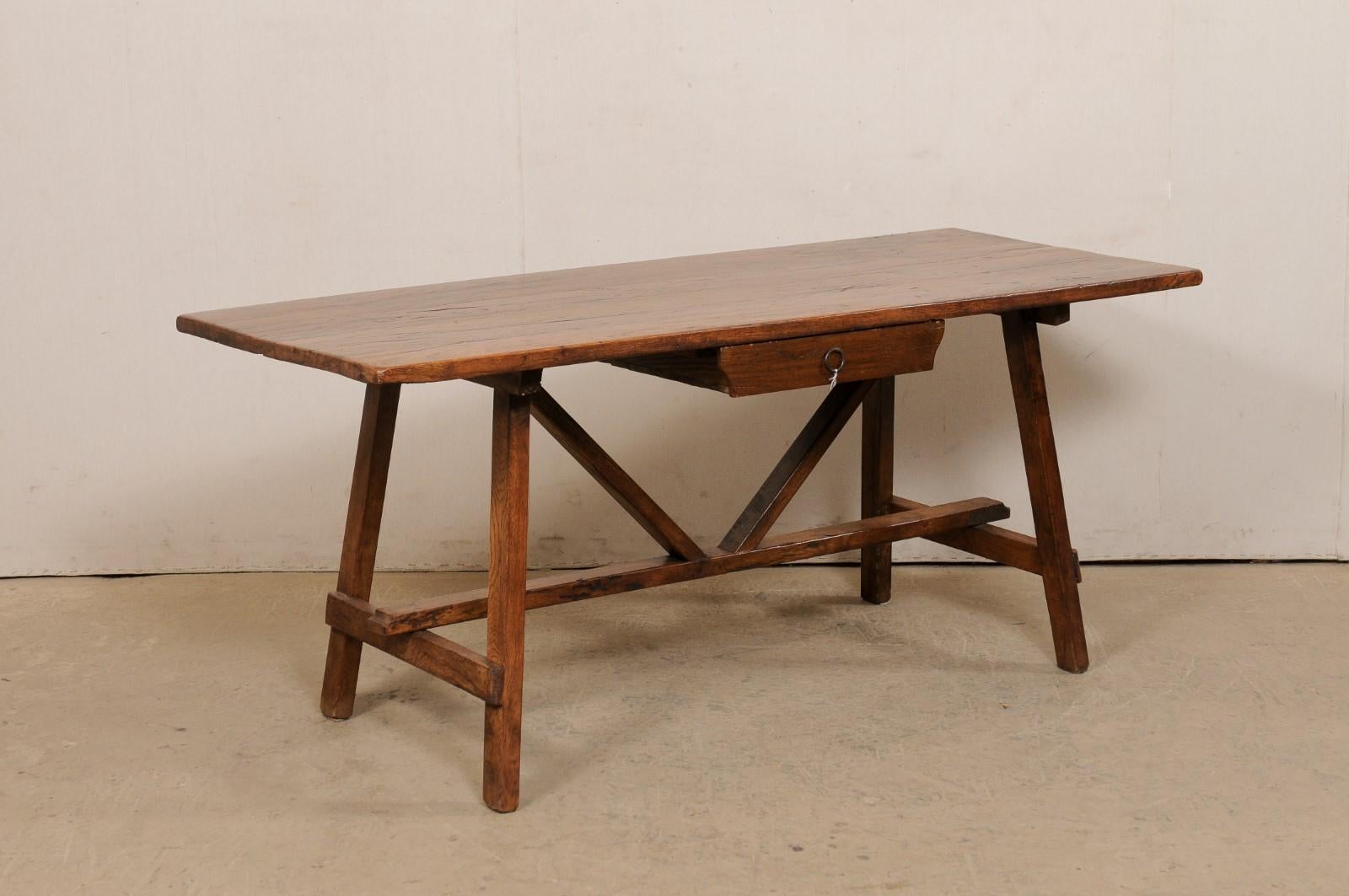 An Italian walnut wood table from the early 18th century. This antique table from Italy has a rectangular-shaped top (with single drawer set at one long side at center), which is raised on a pair of tilted, saw-horse style legs at either far end,