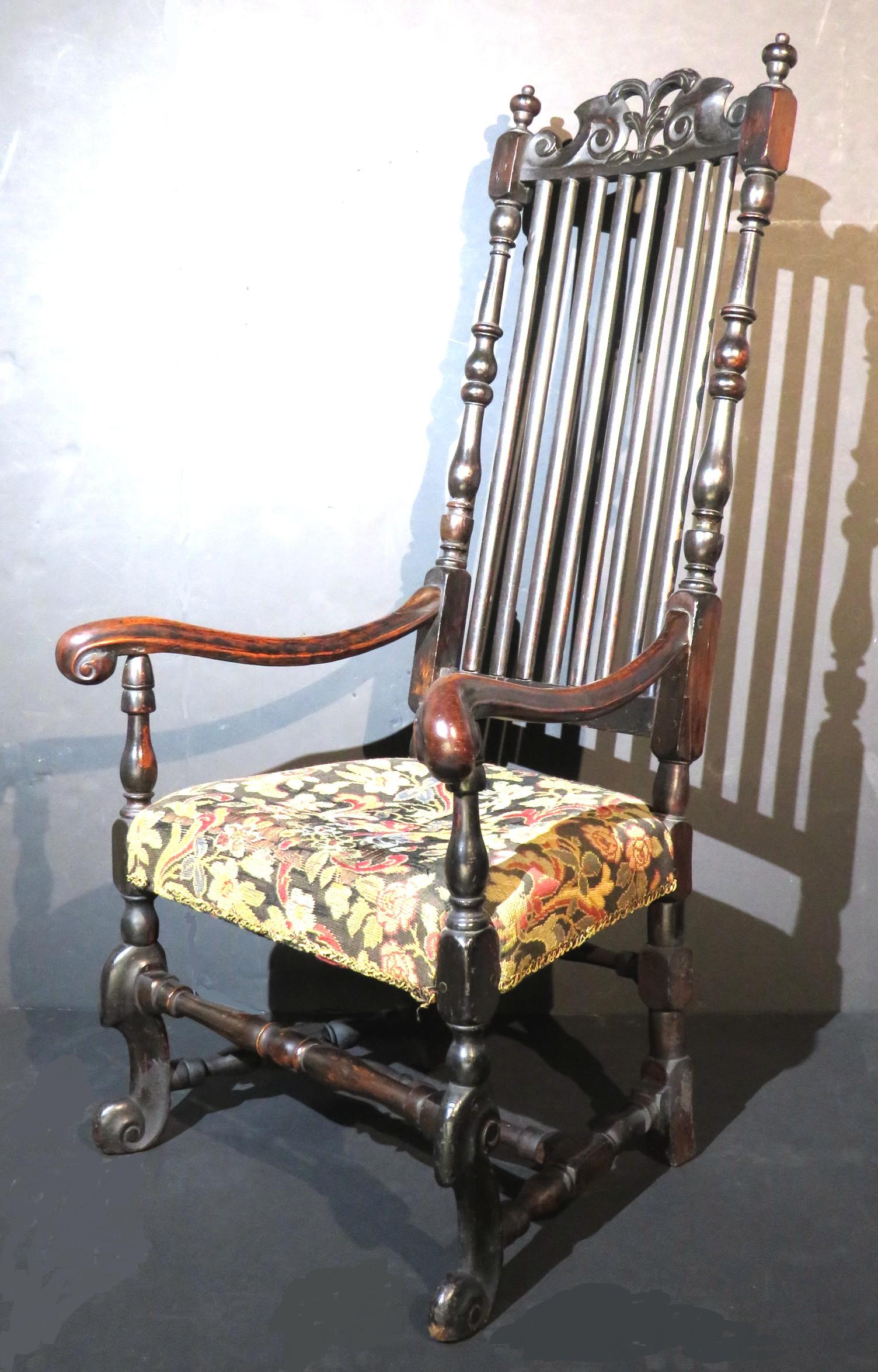 The peg-constructed maple frame featuring a richly carved crest rail with scrolled & foliate motifs, over flattened vertical splats sided by stile supports. The hand embroidered 'gros-point' seat is sided by carved down-swept armrests terminating to