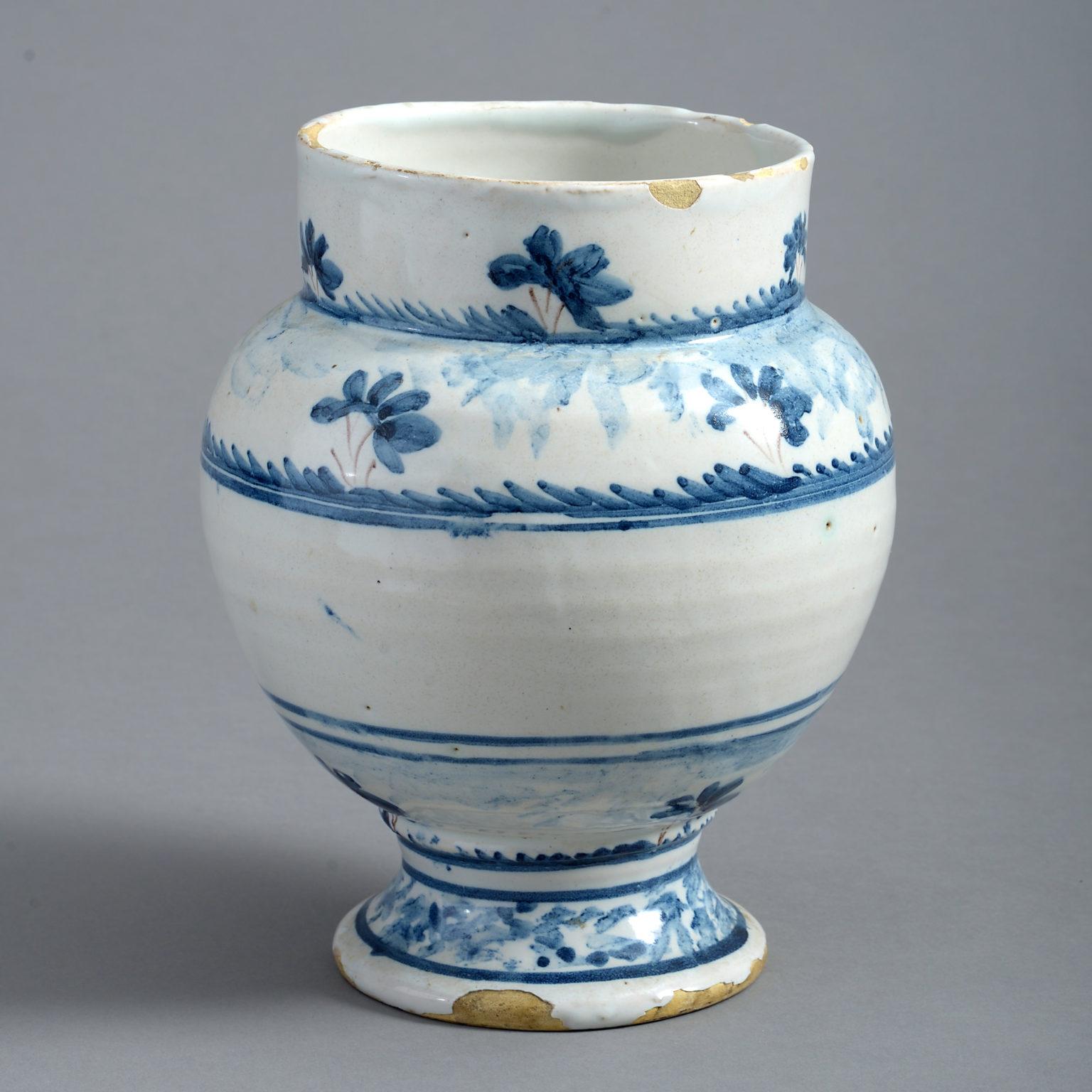 An early 18th century blue and white delft pottery vase, of generous form and decorated sparingly with a stylised landscape of trees in blue and magenta glazes upon a white ground.