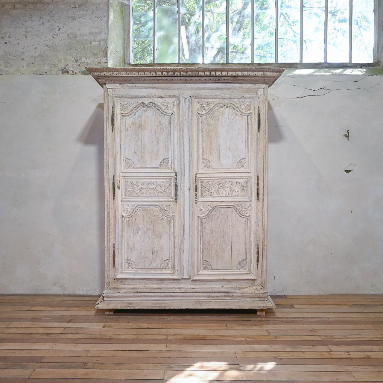 A large scale early 18th century Louis XIV bleached oak armoire. Of large proportions. Displaying a pair of elegantly carved doors - depicting acanthus leaves, flowers and swags. The sides consist of three panels: a horizontal rectangle in between