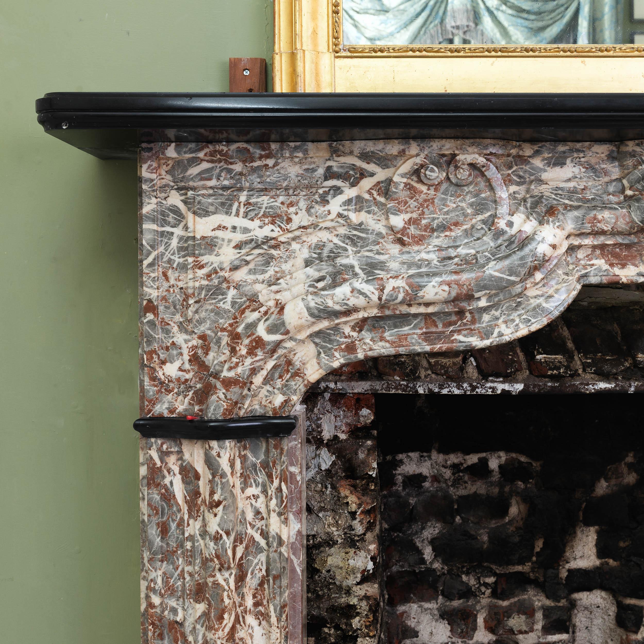 An early eighteenth century French Rance marble fireplace - a transitional Louis XIV/Louis XV surround - the moulded Belgian Black marble shelf above boldly shaped and moulded frieze with panelled spandrels.

Dimensions:	134.5cm (53