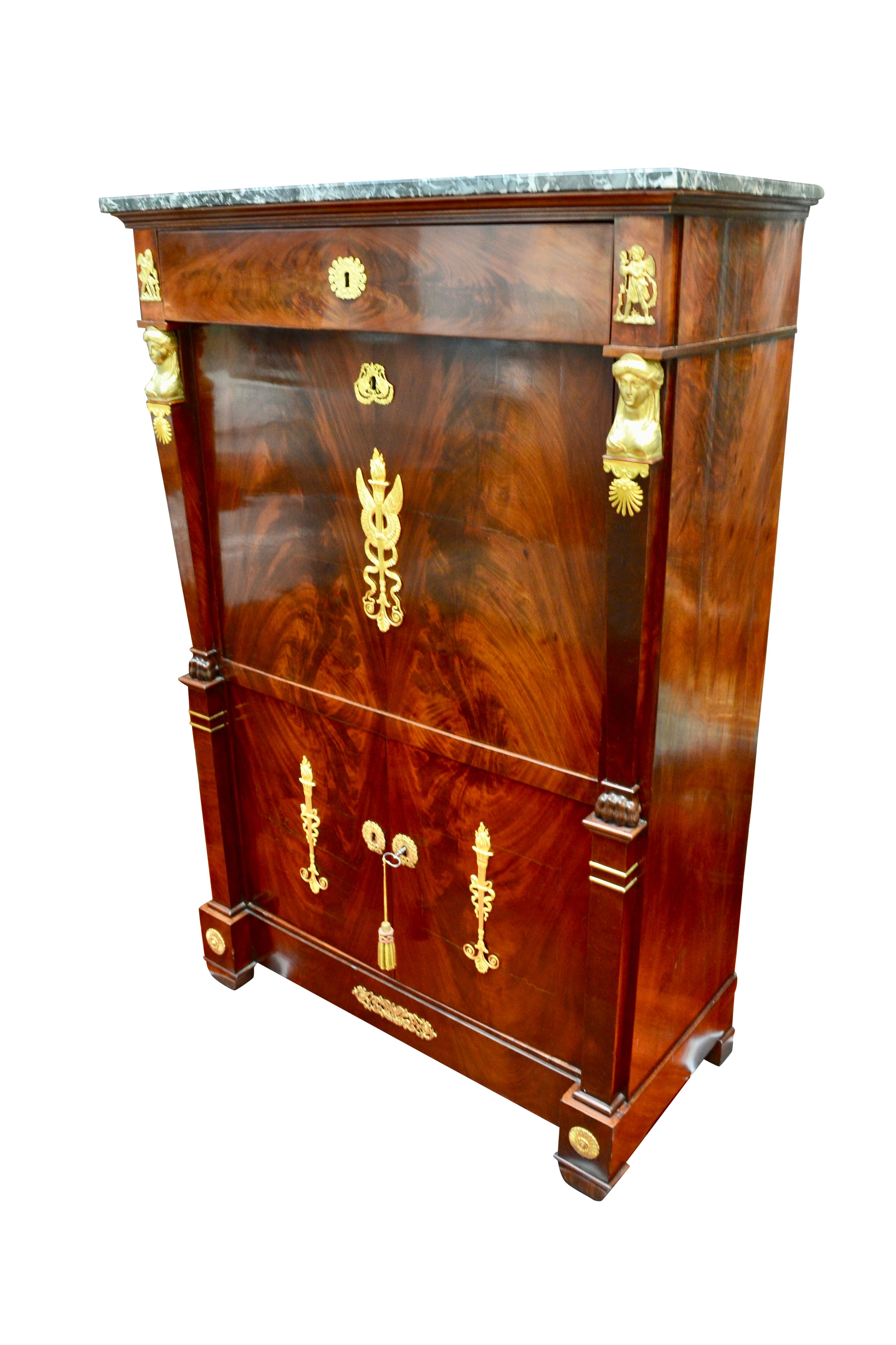 A period French Empire fall front desk referred to as an Abattant. The case is constructed in a rich dark mahogany. There is a single drawer below the mottled grey marble top, below that is the fall front door which is flanked by columns surmounted