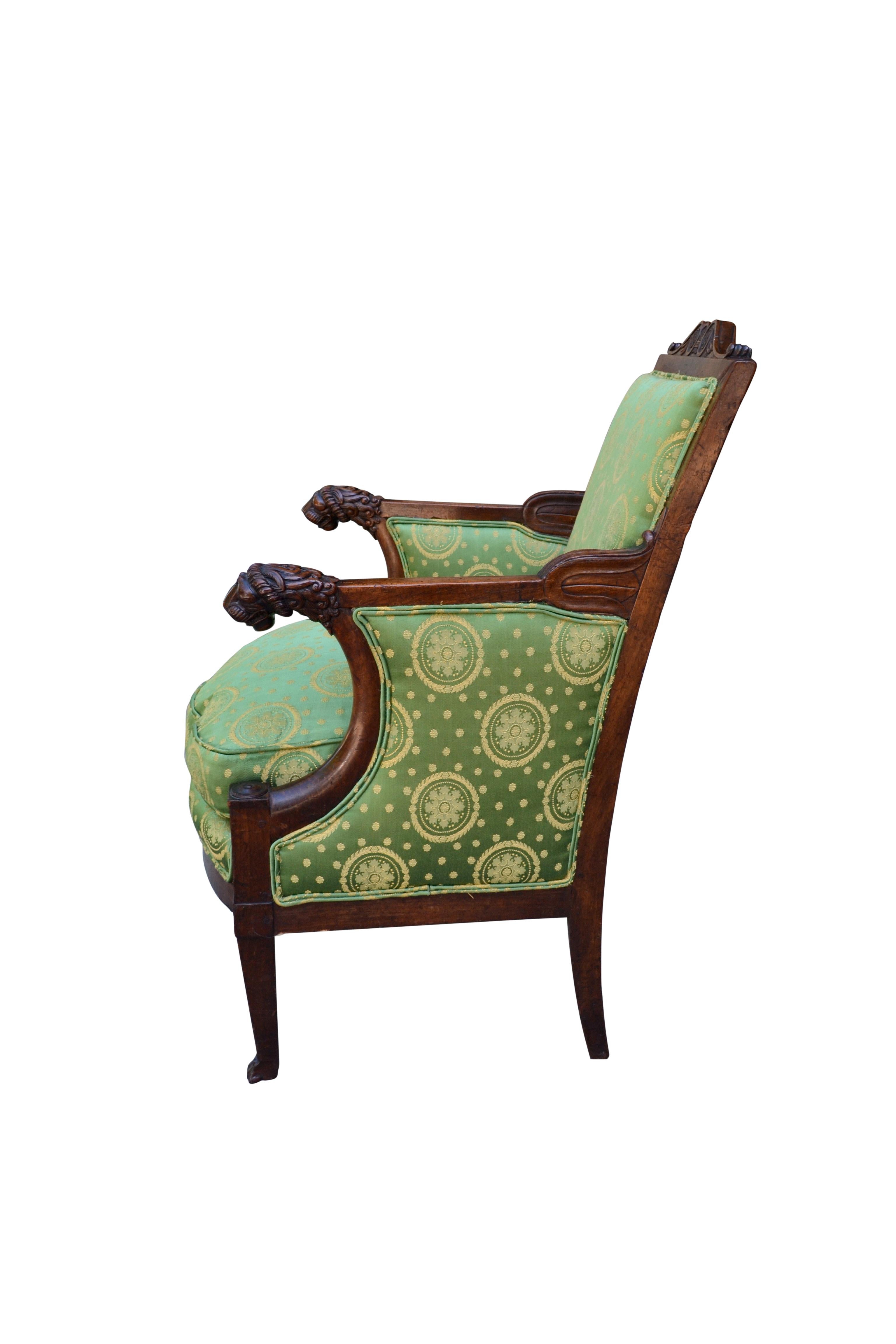 A period French Empire mahogany armchair with carved lion heads to the arms and lion's paw feet to the legs, upholstered in French Empire style green silk fabric.
  
