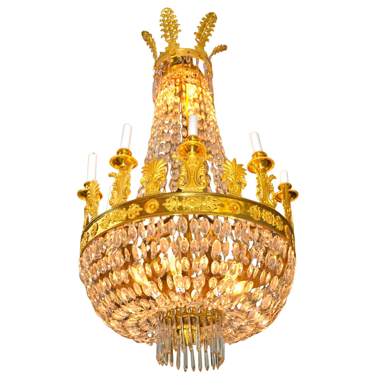 Lustre d'époque Empire français en cristal et bronze doré avec neuf bougies. Le lustre comporte une partie supérieure décorée de guirlandes de cristal et de grandes palmettes dorées, le corps étant suspendu par des rangées de cristaux gradués en