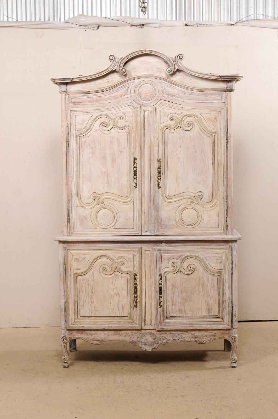 A tall French carved and painted wood storage cabinet from the early 19th century. This antique buffet à deux-corps from France features a delicately arched and molded center top pediment with curly volute accents, a pair of upper decoratively